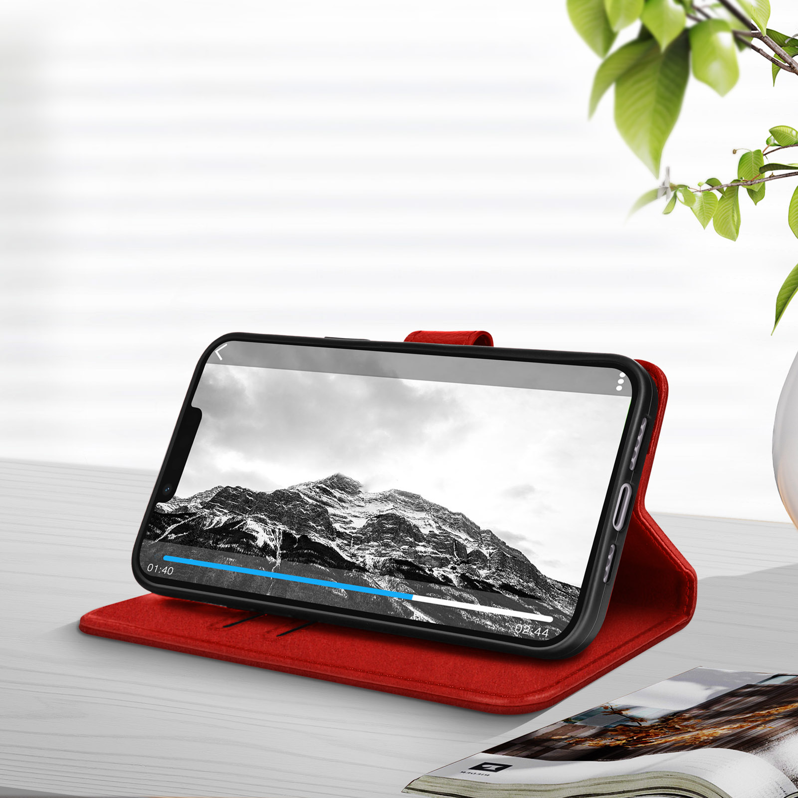 Een telefoon in een rode hoes toont een video met een berglandschap, open op een bureau.