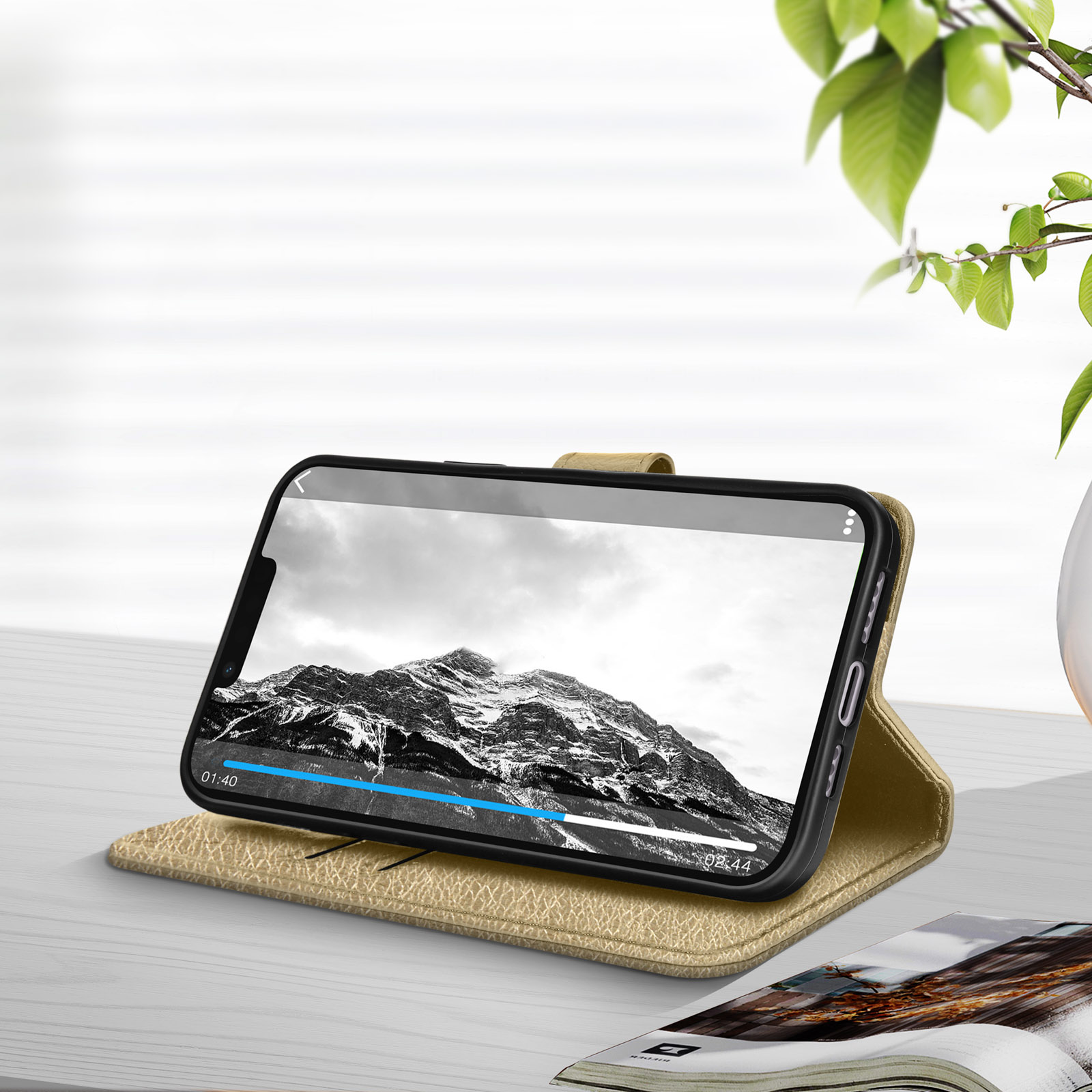 Telefono che riproduce un video su un supporto, con sfondo panoramico. Presenti anche una foglia e un libro.