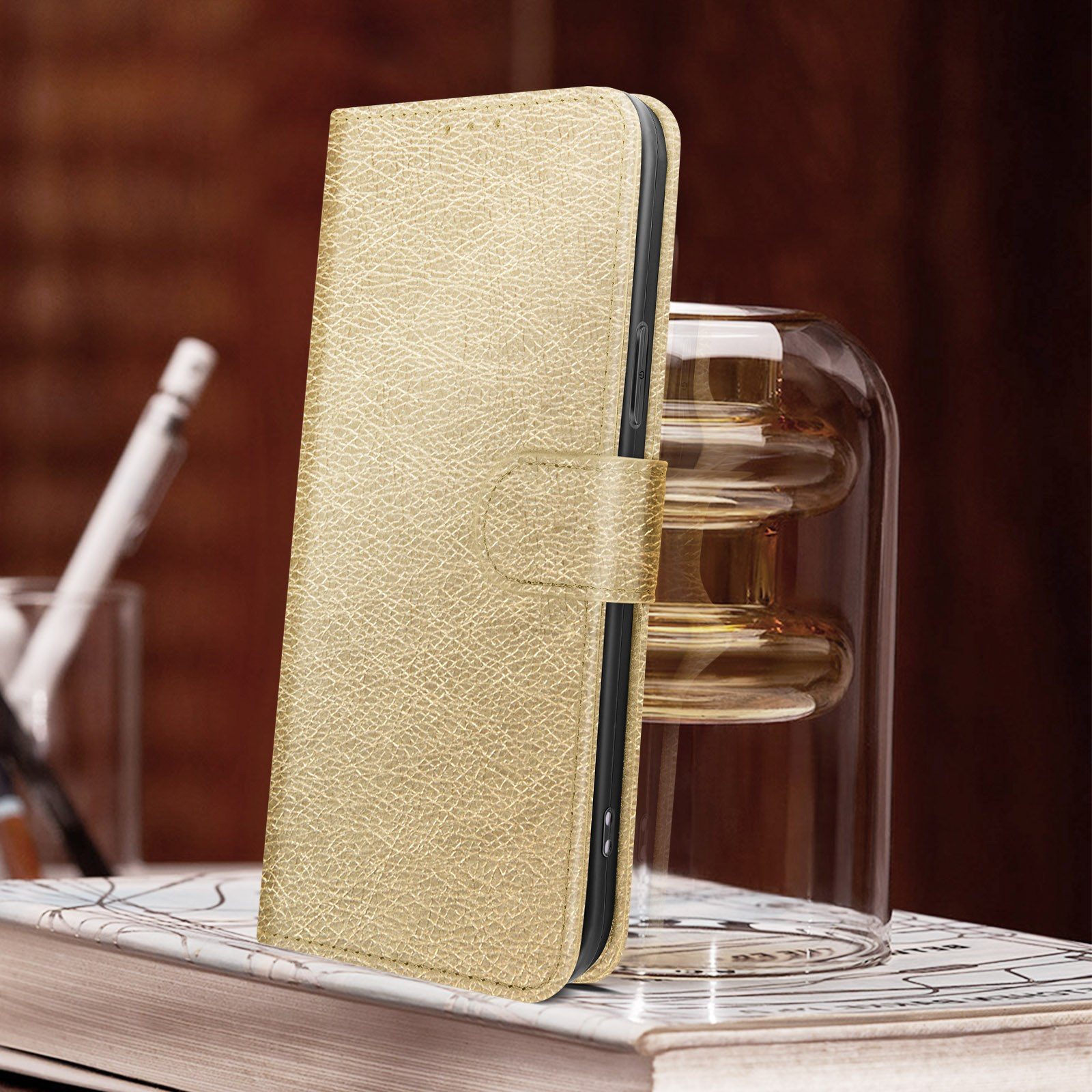 Eine goldene Handyhülle, geöffnet, auf einem Buch gegen eine Glasvase.