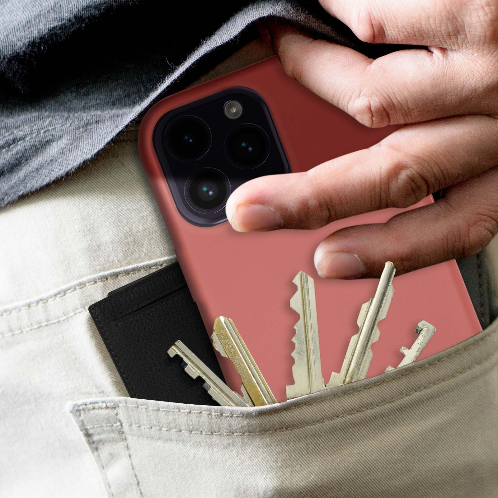 De hand van een persoon in een zak met sleutels en een telefoon in een rode hoes.