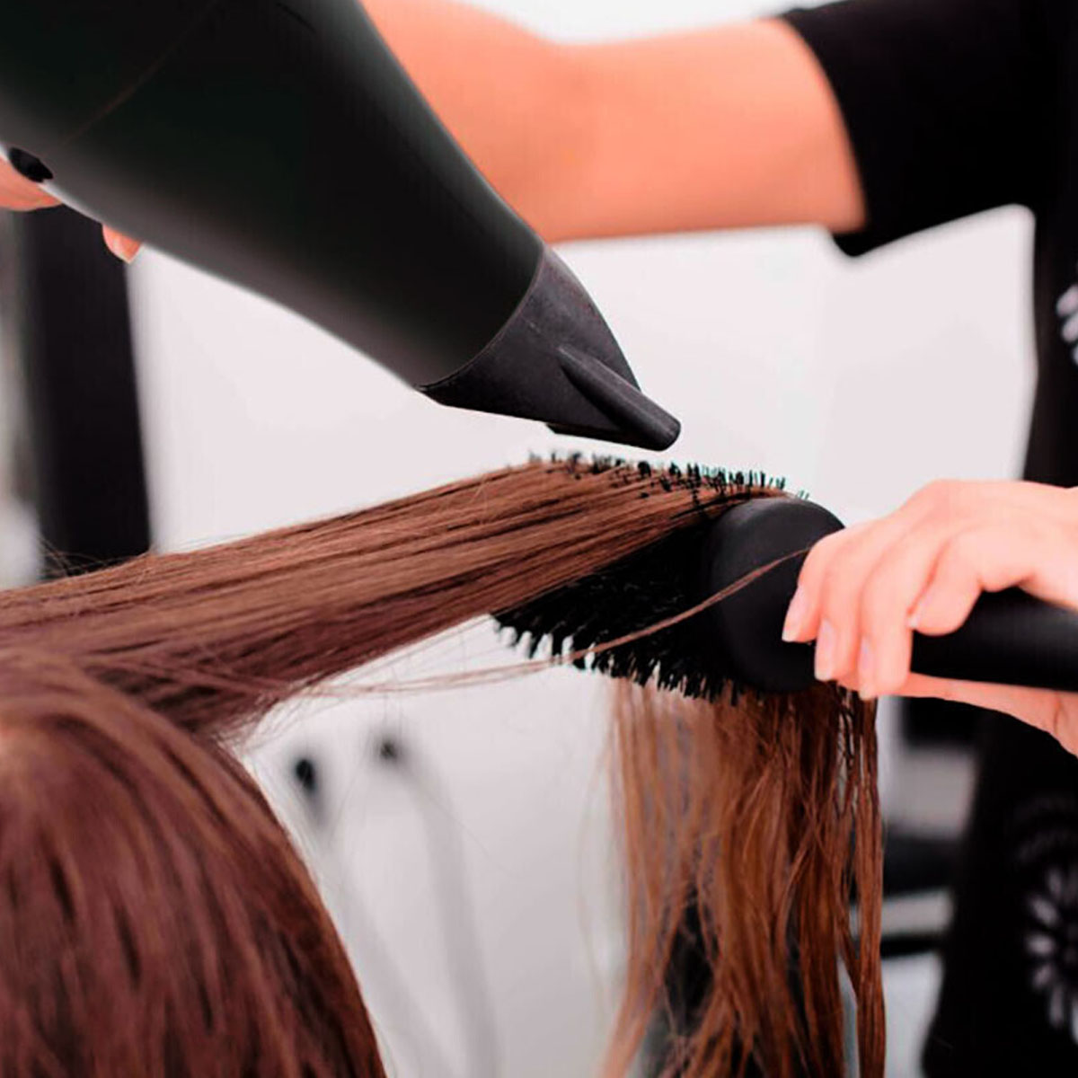 Peluquero usando secador y cepillo sobre cabello castaño. El enfoque está en el cabello.