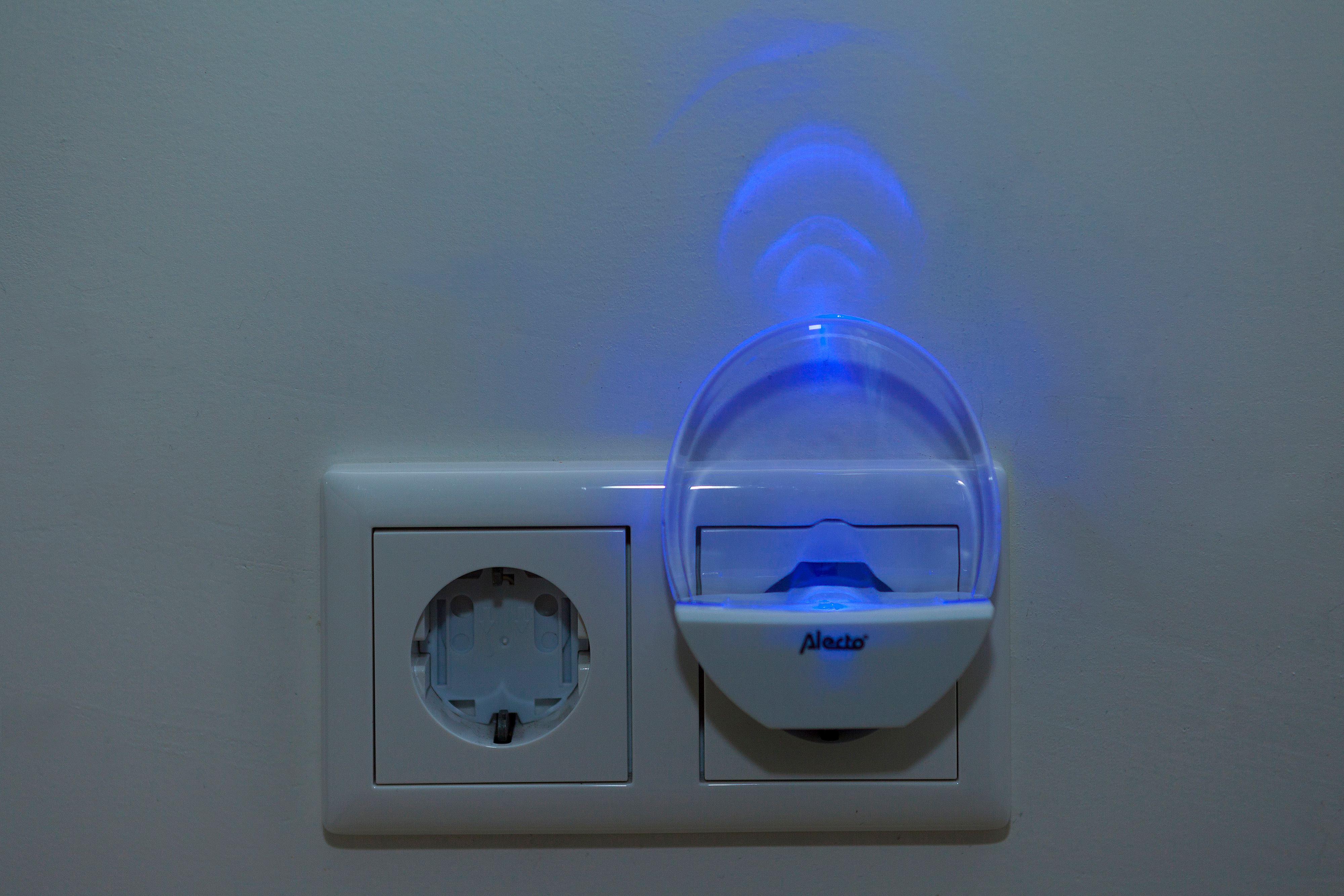 Gniazdko ścienne z wpiętą lampką nocną. Lampka nocna jest biała i emituje niebieską poświatę.