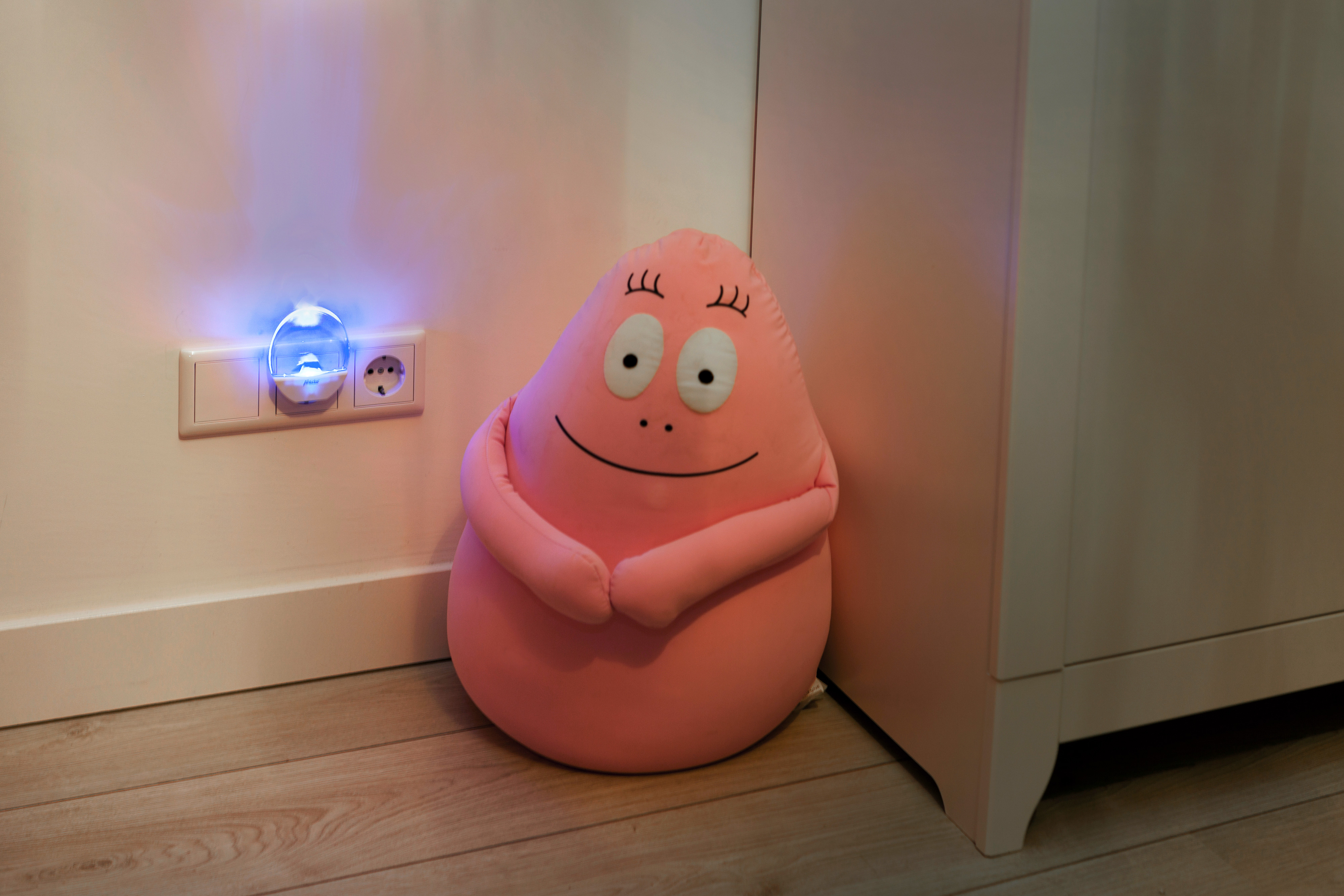 Różowa, uśmiechnięta pluszowa zabawka z kreskówki. Wtyczka i gniazdo ścienne.