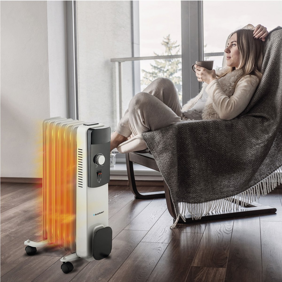Kobieta relaksuje się obok grzejnika. Trzyma kubek. Grzejnik jest włączony.
