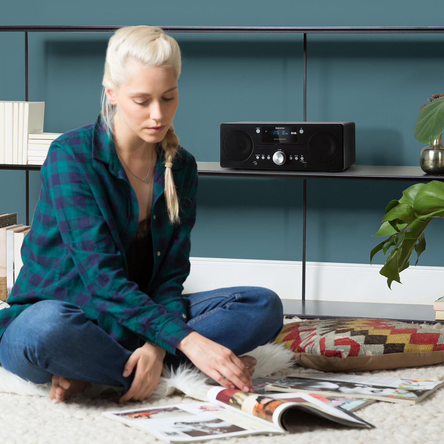 Frau sitzt mit Radio. Liest Zeitschriften auf einem Teppich.