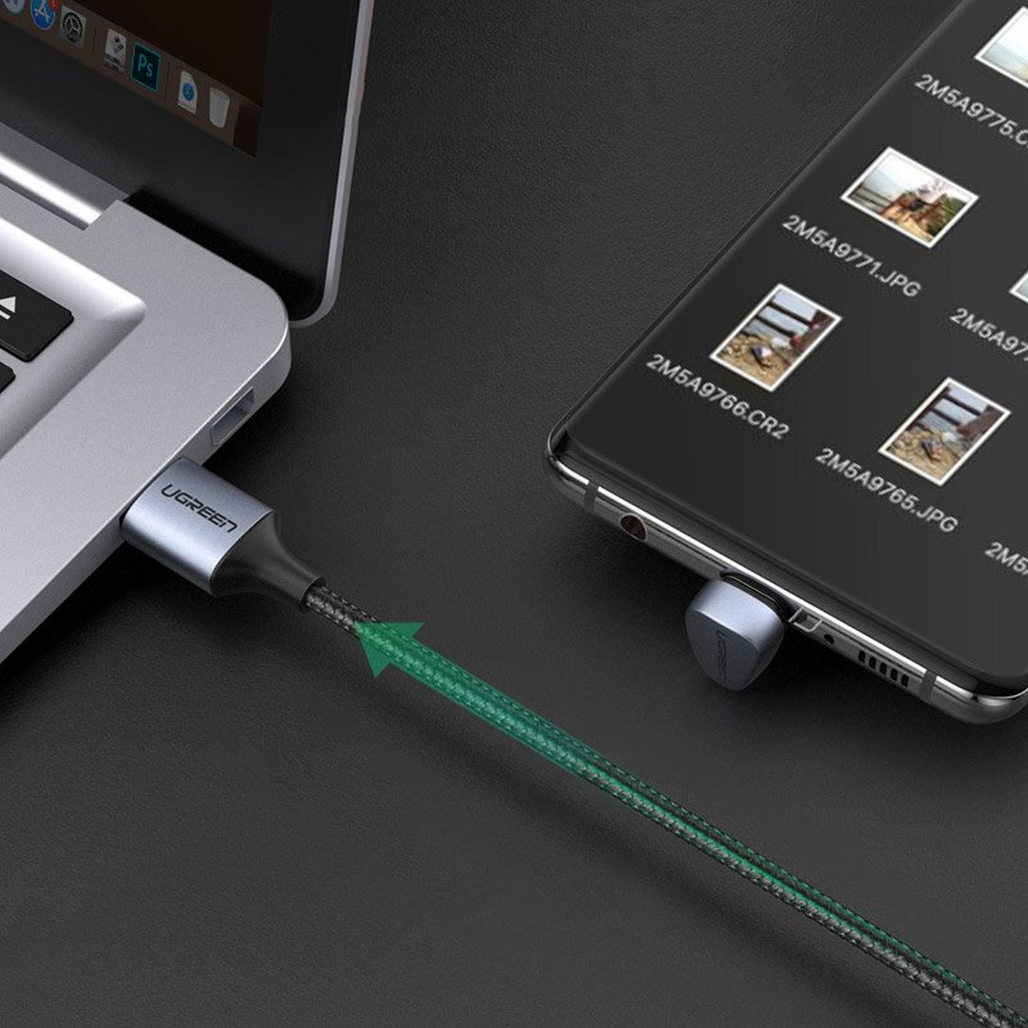 Ein USB-C-Kabel verbindet einen Laptop und ein Smartphone. Das Kabel ist grün und schwarz. Der Hintergrund ist unscharf.