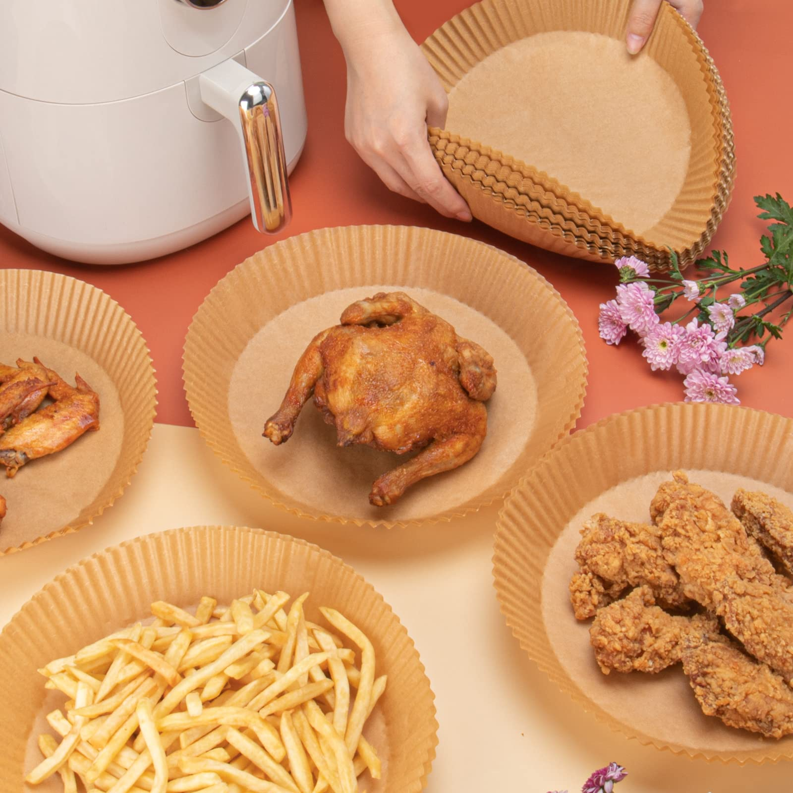Heißluftfritteuse mit Speisen in Papiereinlagen. Hähnchen, Pommes und Wings sind sichtbar.