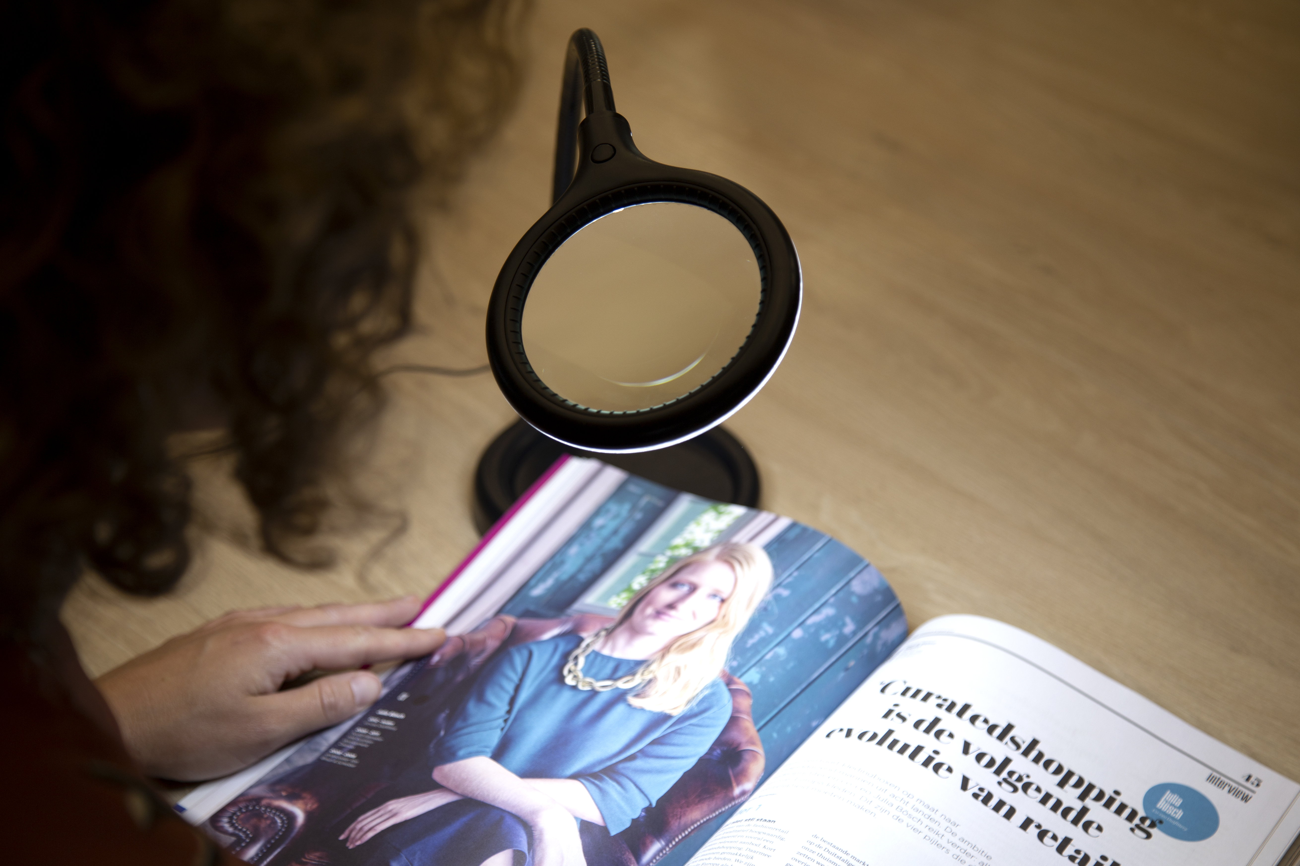 Person liest Zeitschrift mit Lupe über der Zeitschrift.