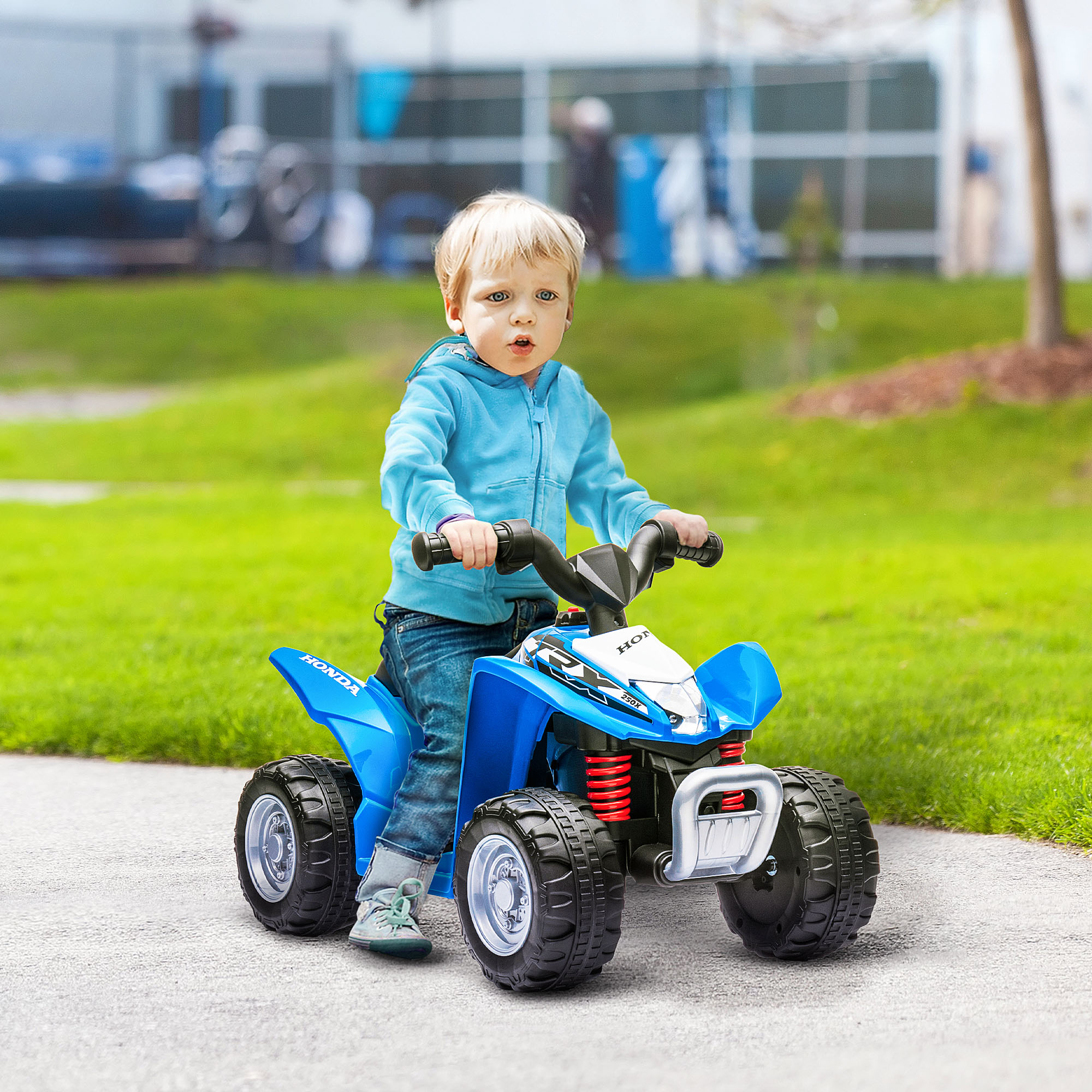 Un bambino cavalca un quad giocattolo blu su un sentiero pavimentato, erba verde sullo sfondo.