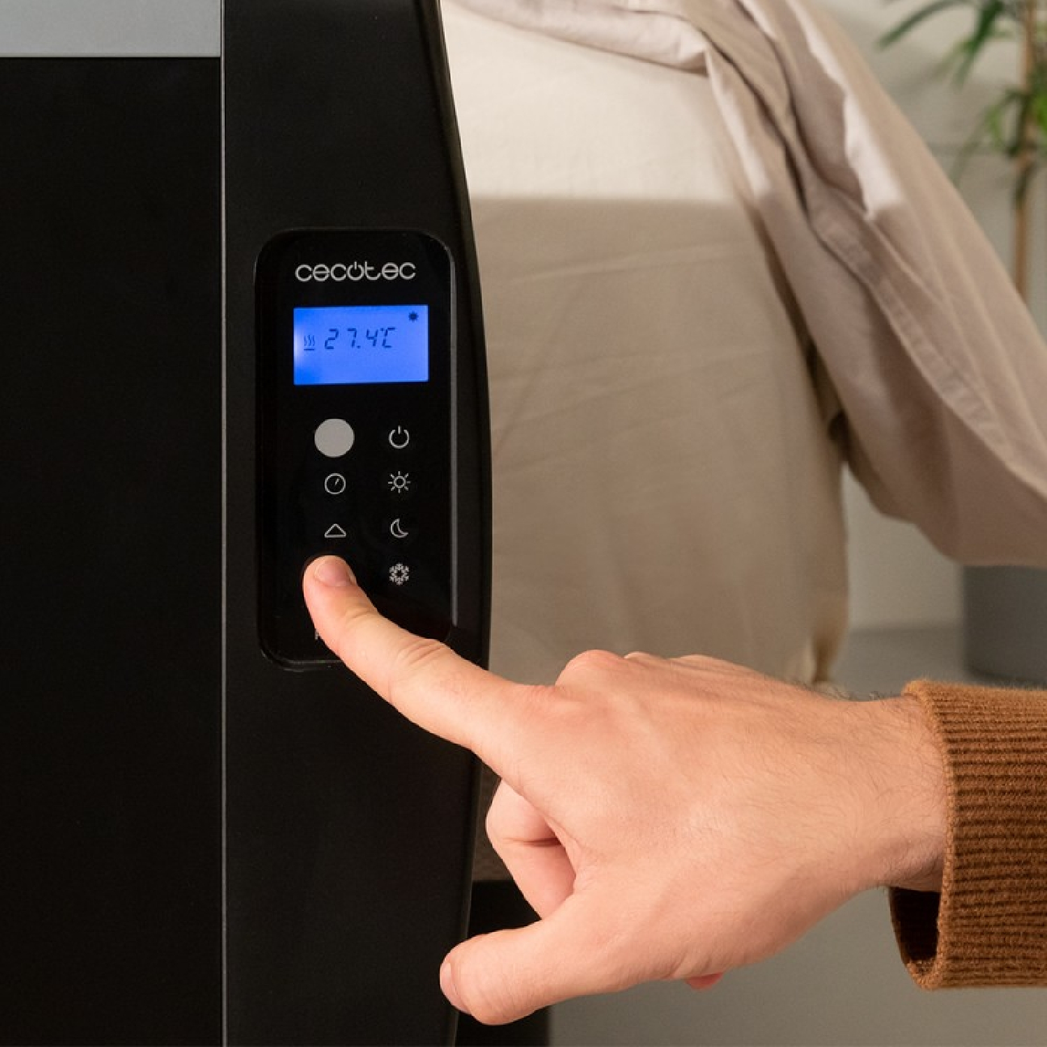 Ręka wskazująca na czarny panel sterowania, z grzejnikiem w tle.