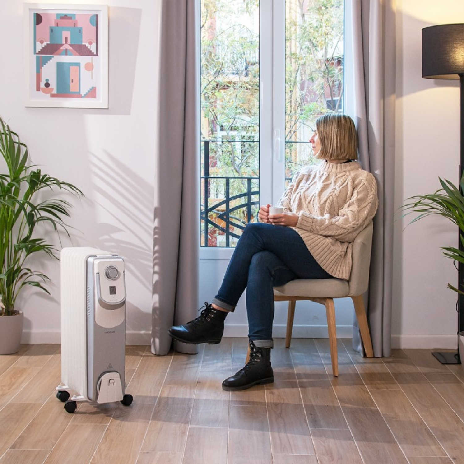 Kobieta siedząca na krześle przy oknie z grzejnikiem olejowym przed nią.