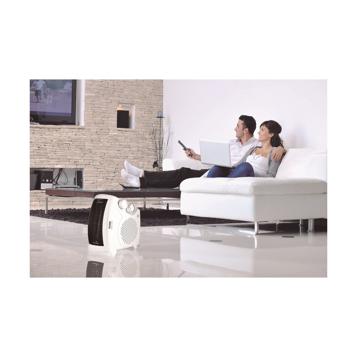 Una pareja viendo la televisión, con un calefactor blanco delante y un sofá blanco detrás.