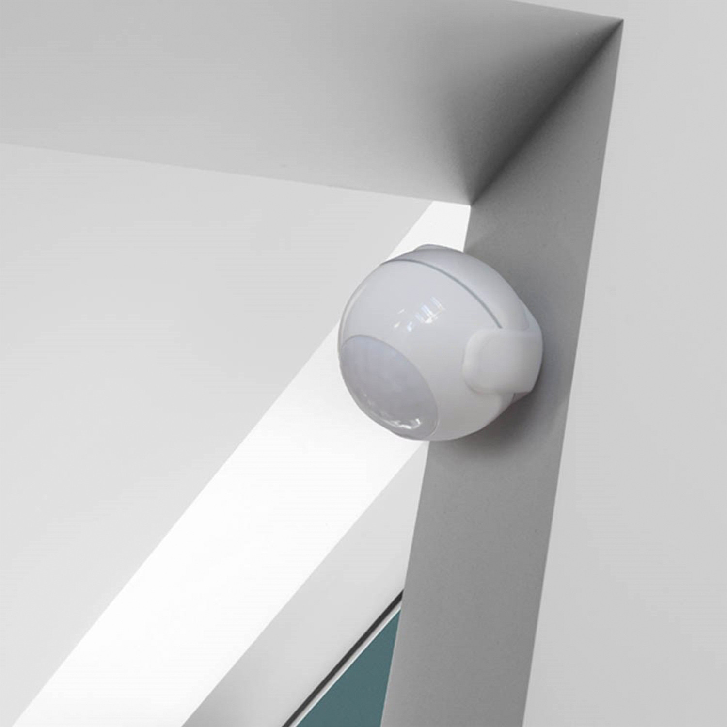 Sensor de movimiento blanco montado en pared blanca, con esquina al fondo.