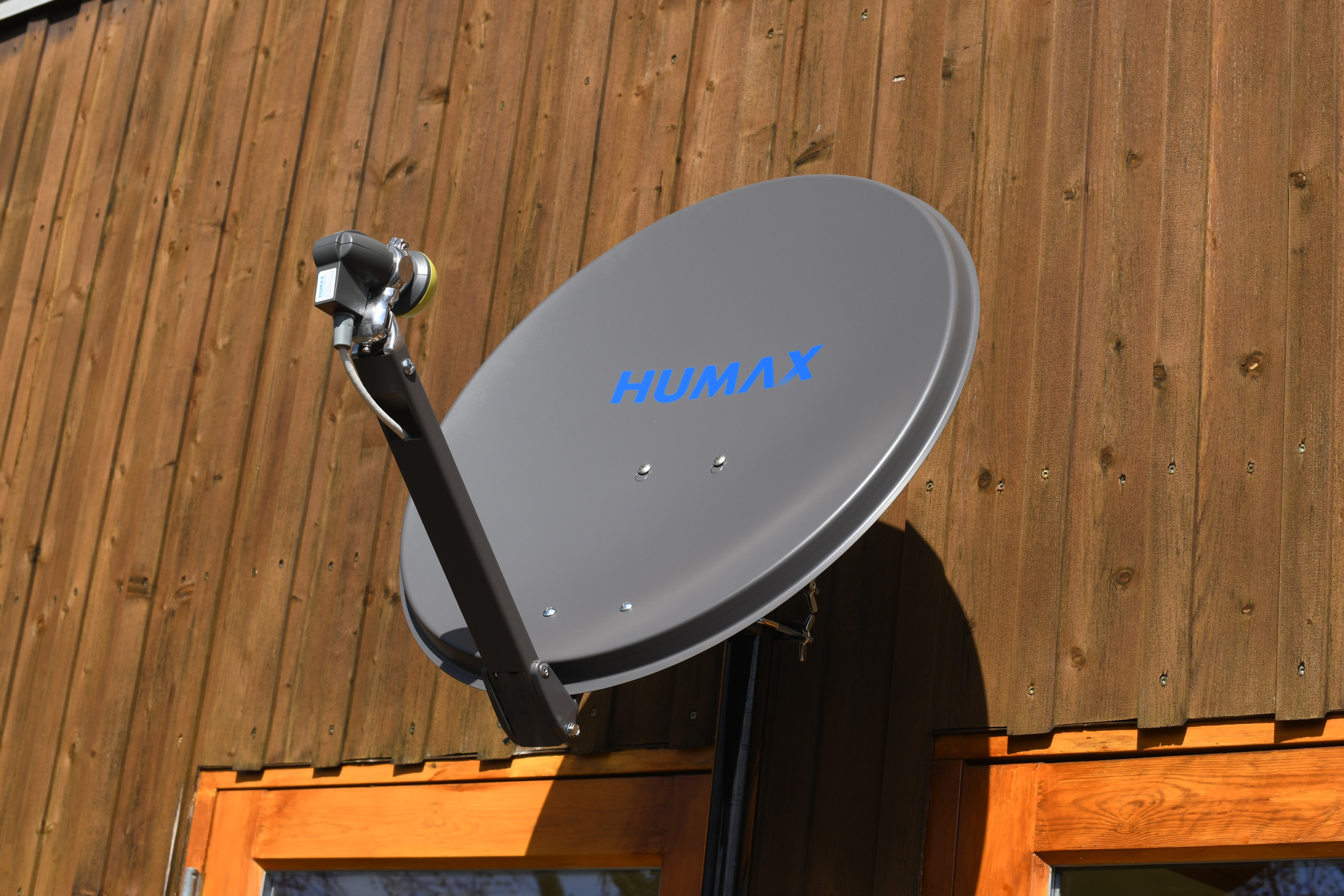 Eine graue Satellitenschüssel an einer Holzwand, mit dem Wort HUMAX in Blau.