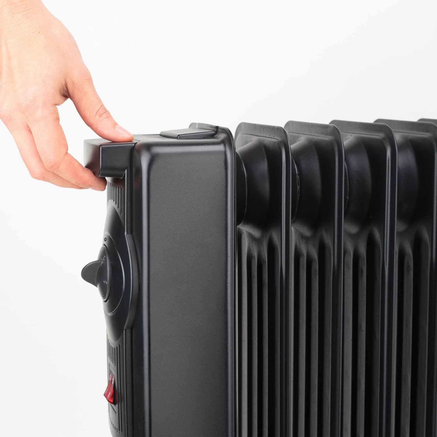 Ręka obracająca czarne pokrętło grzejnika olejowego. Białe tło, widok z boku.