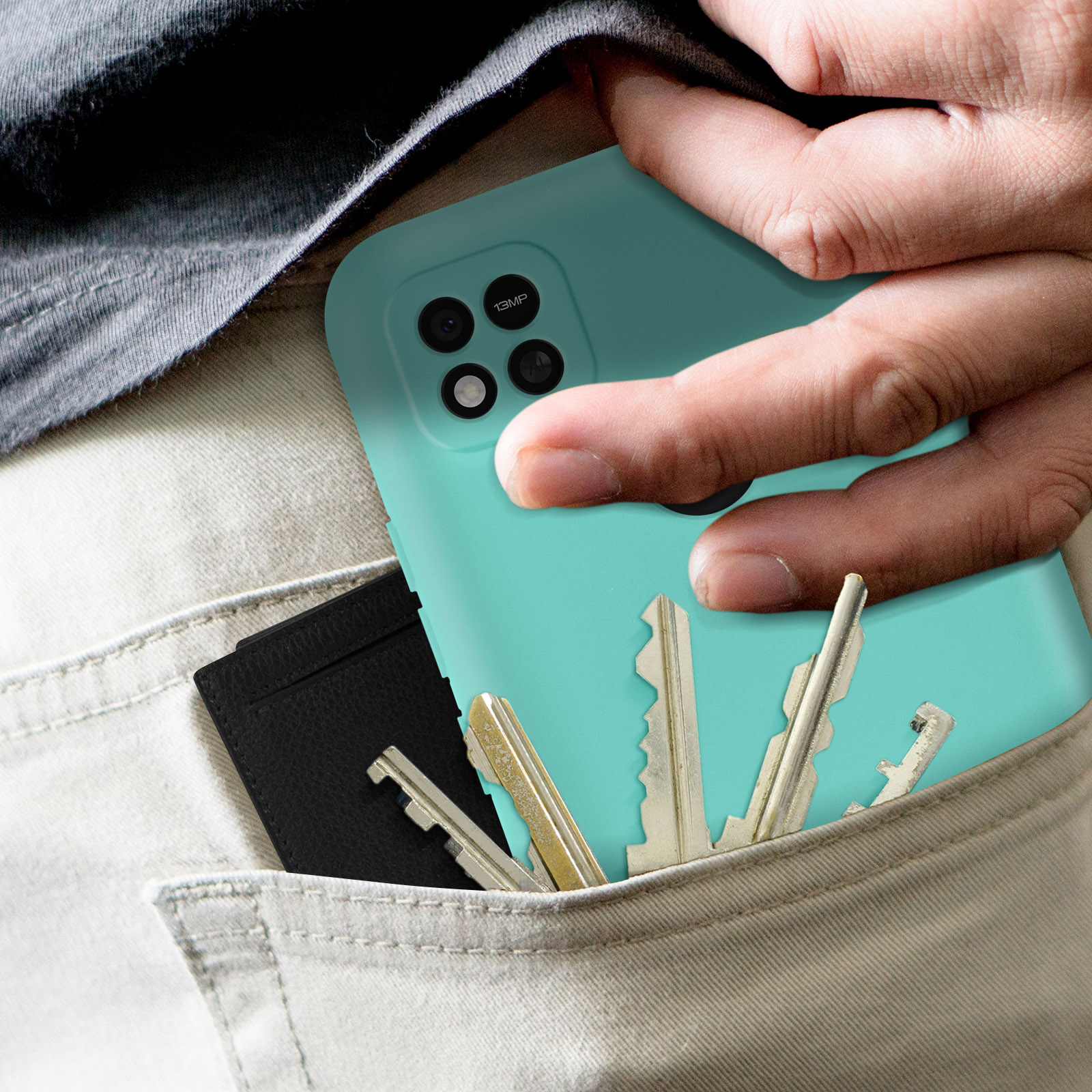 Main dans la poche tenant une coque de téléphone teal avec des clés et un porte-cartes noir.