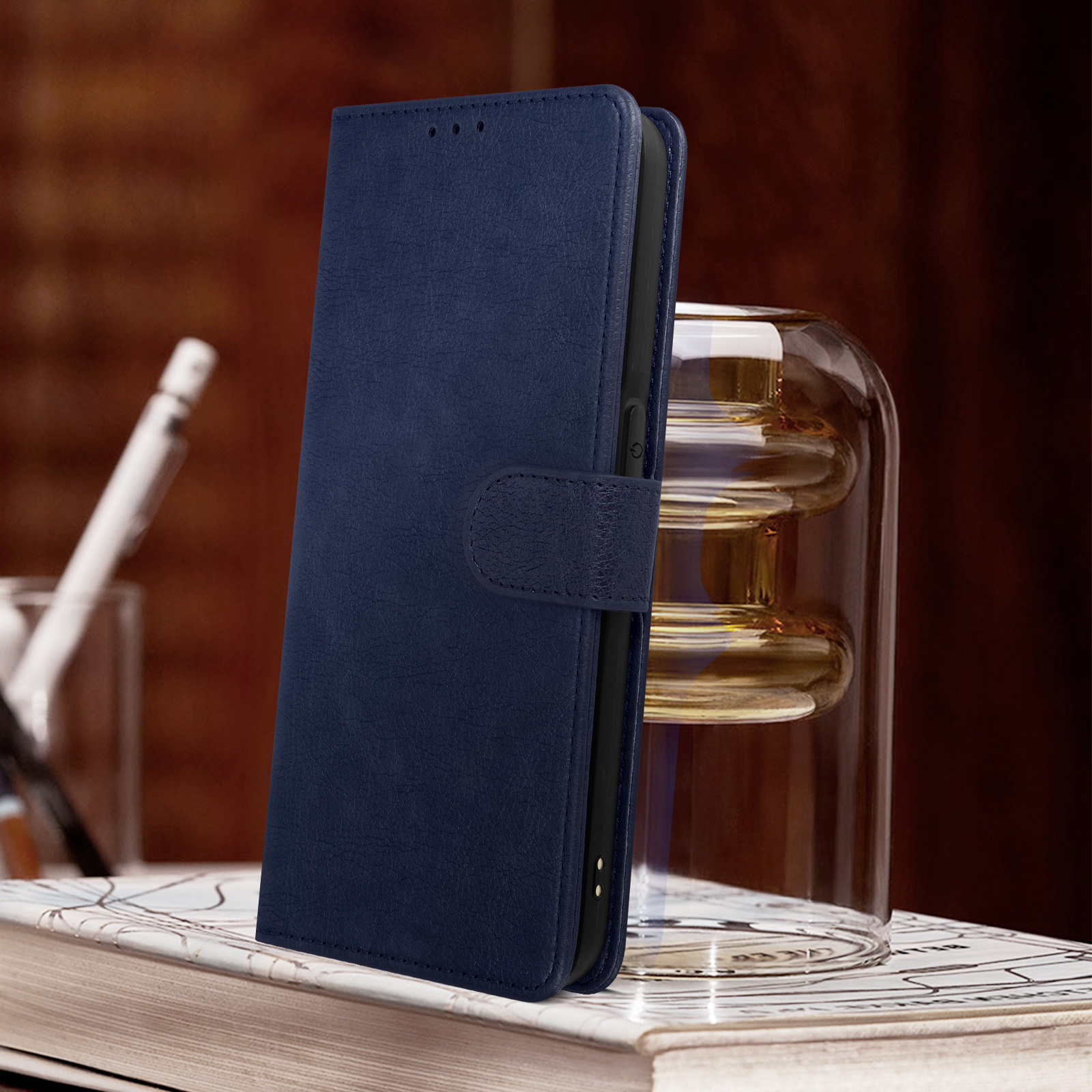 Eine marineblaue Handyhülle, offen, mit Telefon darin. Sie liegt auf einem Buch neben einem Glas.