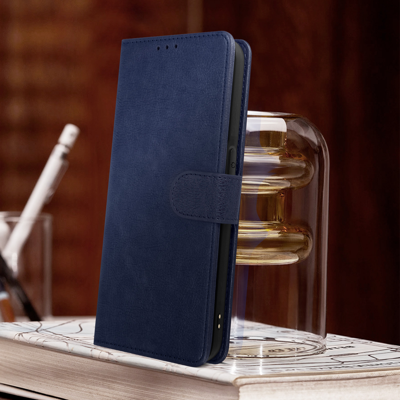 Étui de téléphone bleu avec texture cuir. Avec fermoir, sur un livre, près d'un vase en verre.