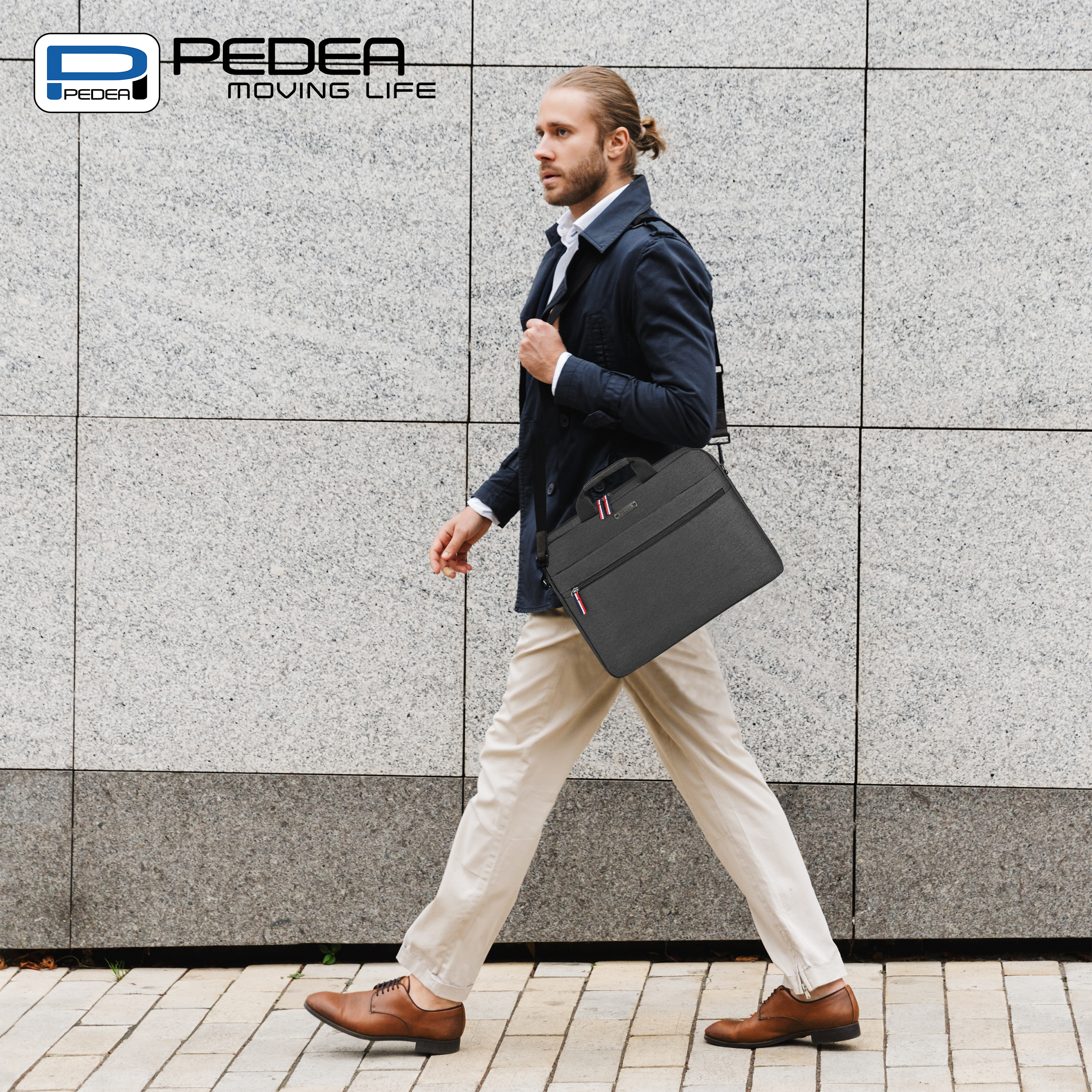 Un uomo cammina su un marciapiede con una borsa nera sulla spalla. La borsa ha un logo.