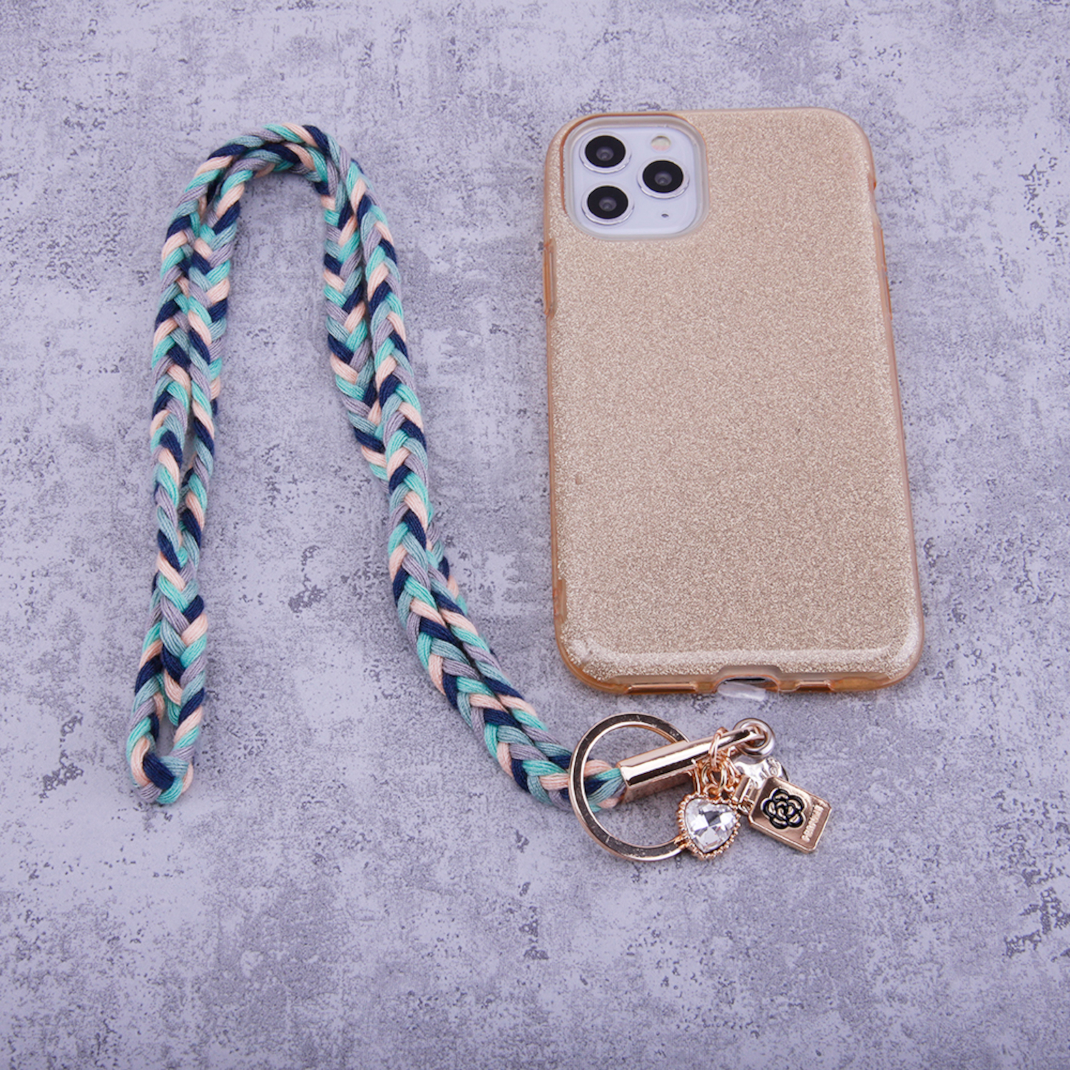 Eine goldene Handyhülle mit mehrfarbig geflochtenem Lanyard. Ein Schlüsselring mit Anhängern ist befestigt.