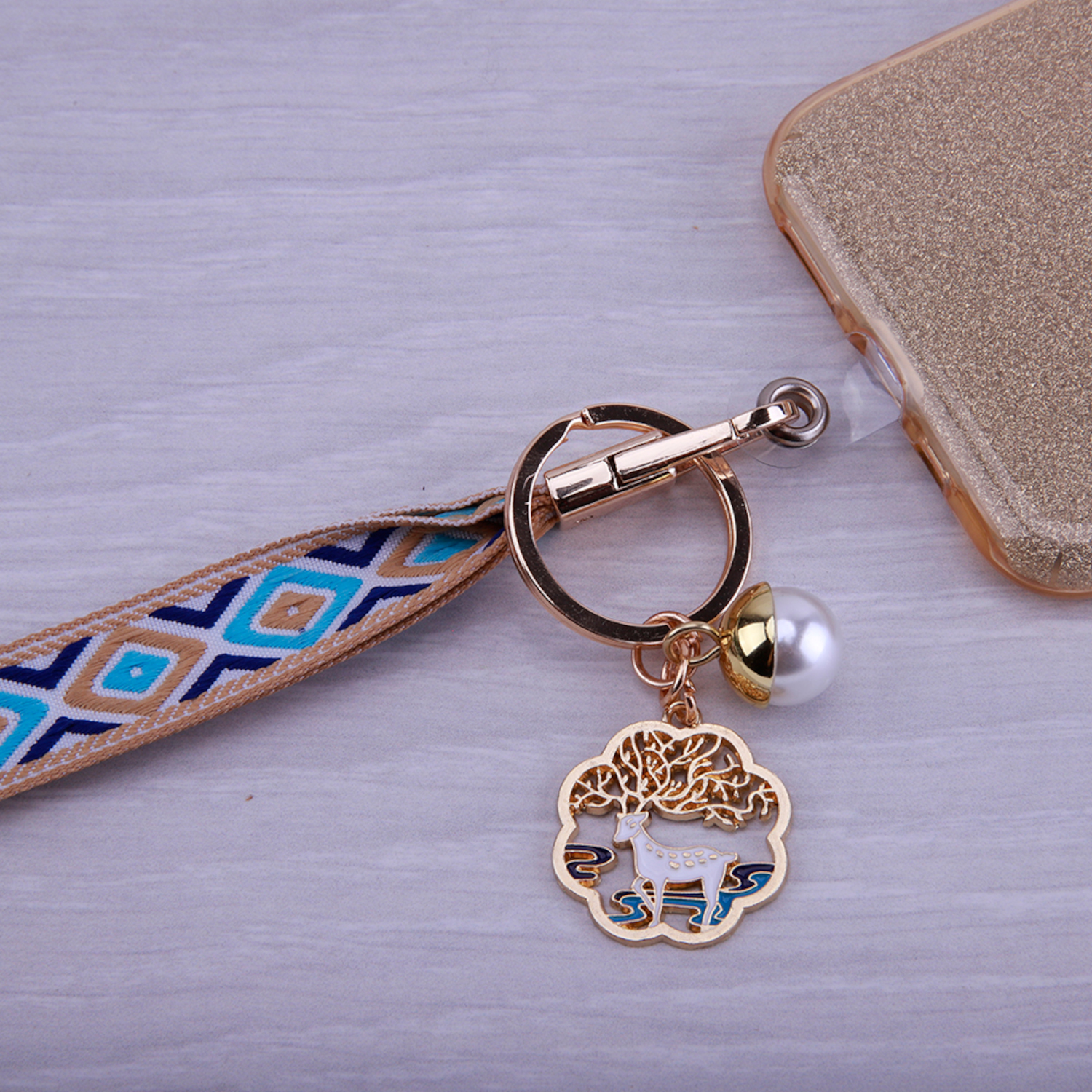 Goldene Handyhülle mit Hirsch-Charm und blau-braunem Riemen. Im Hintergrund ein Handy.