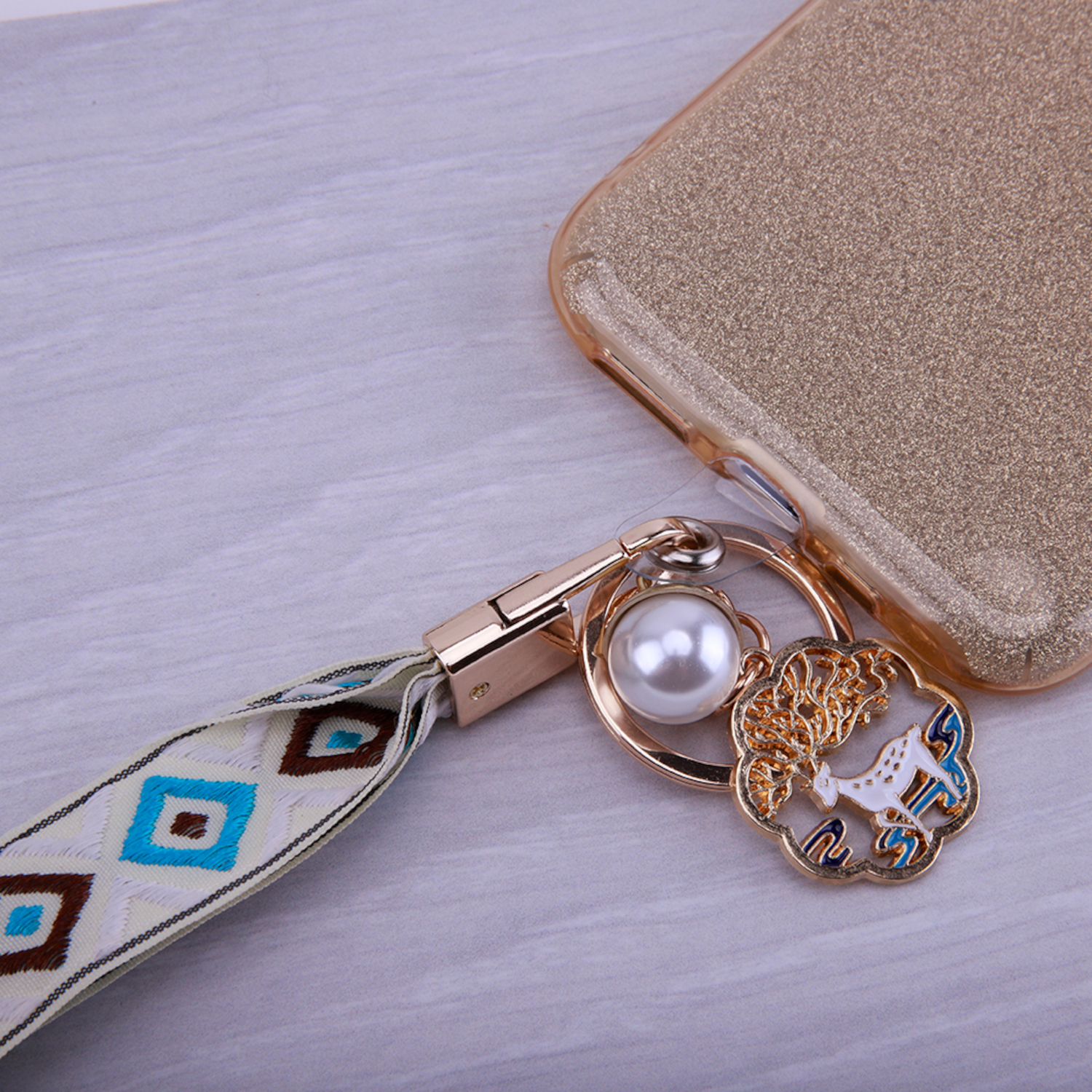 Handyhülle mit goldenem Glitzer-Design, Perlenanhänger und dekorativem Band.