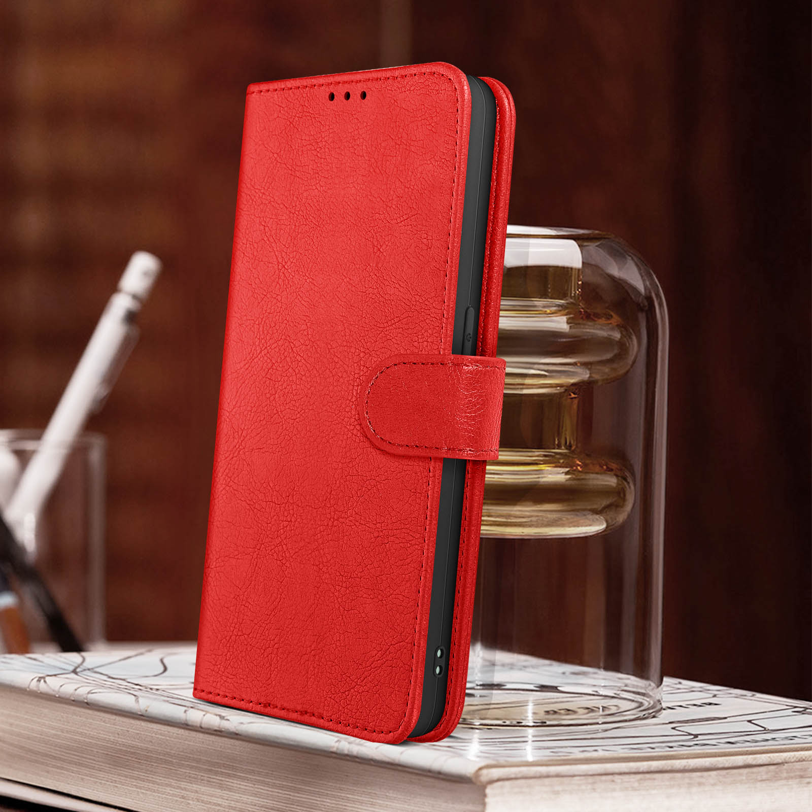 Custodia per telefono in pelle rossa, aperta, su libri. Vaso di vetro trasparente con sfondo sfocato.