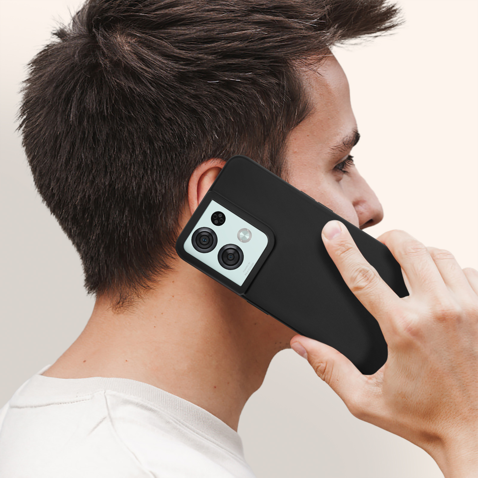 Een man die een zwarte smartphone tegen zijn oor houdt. Hij draagt een wit t-shirt en de achtergrond is effen.