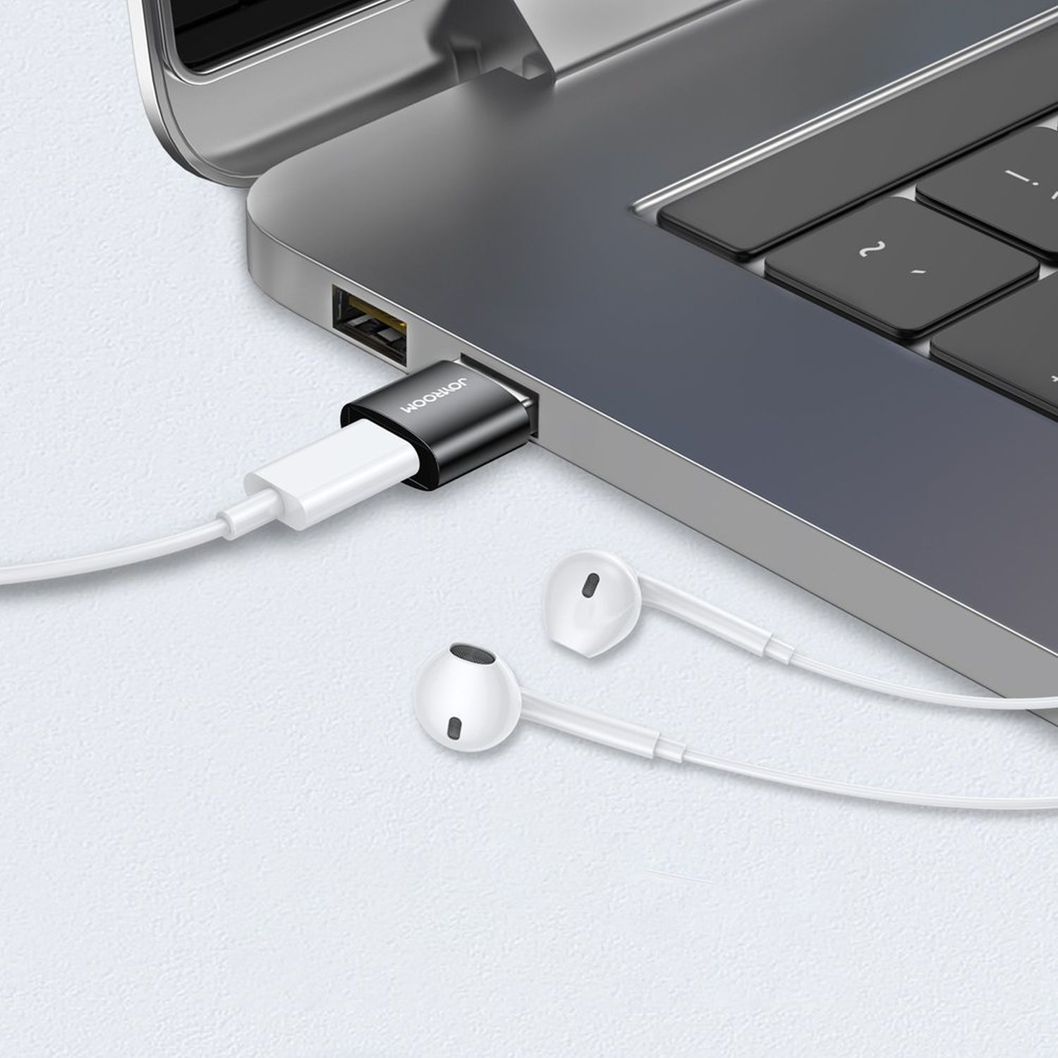 Ein weißer Adapter, der in einen Laptop eingesteckt ist, mit weißen Ohrhörern verbunden.