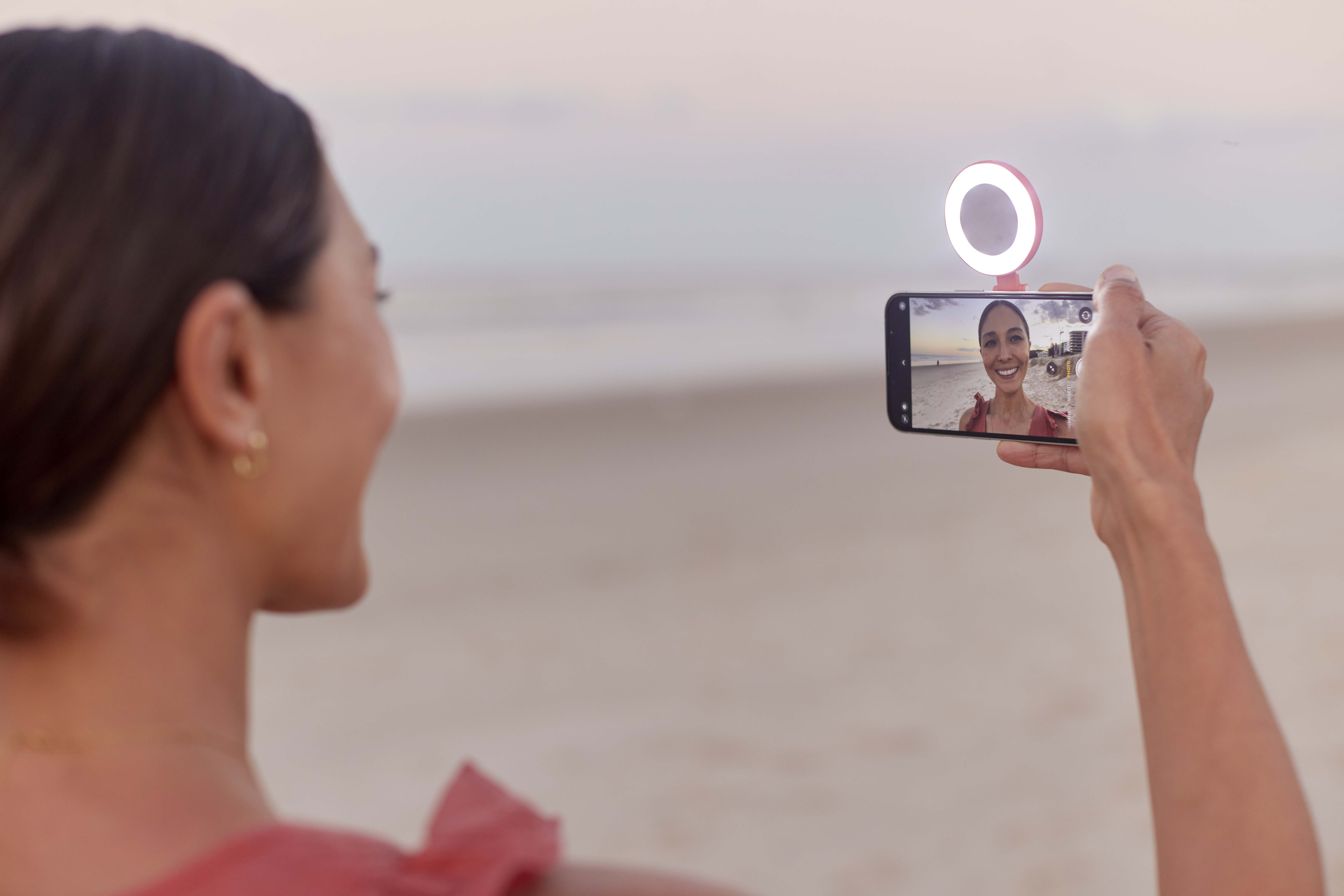 Kadın, sahilde telefon ve halka ışık ile selfie çekiyor.