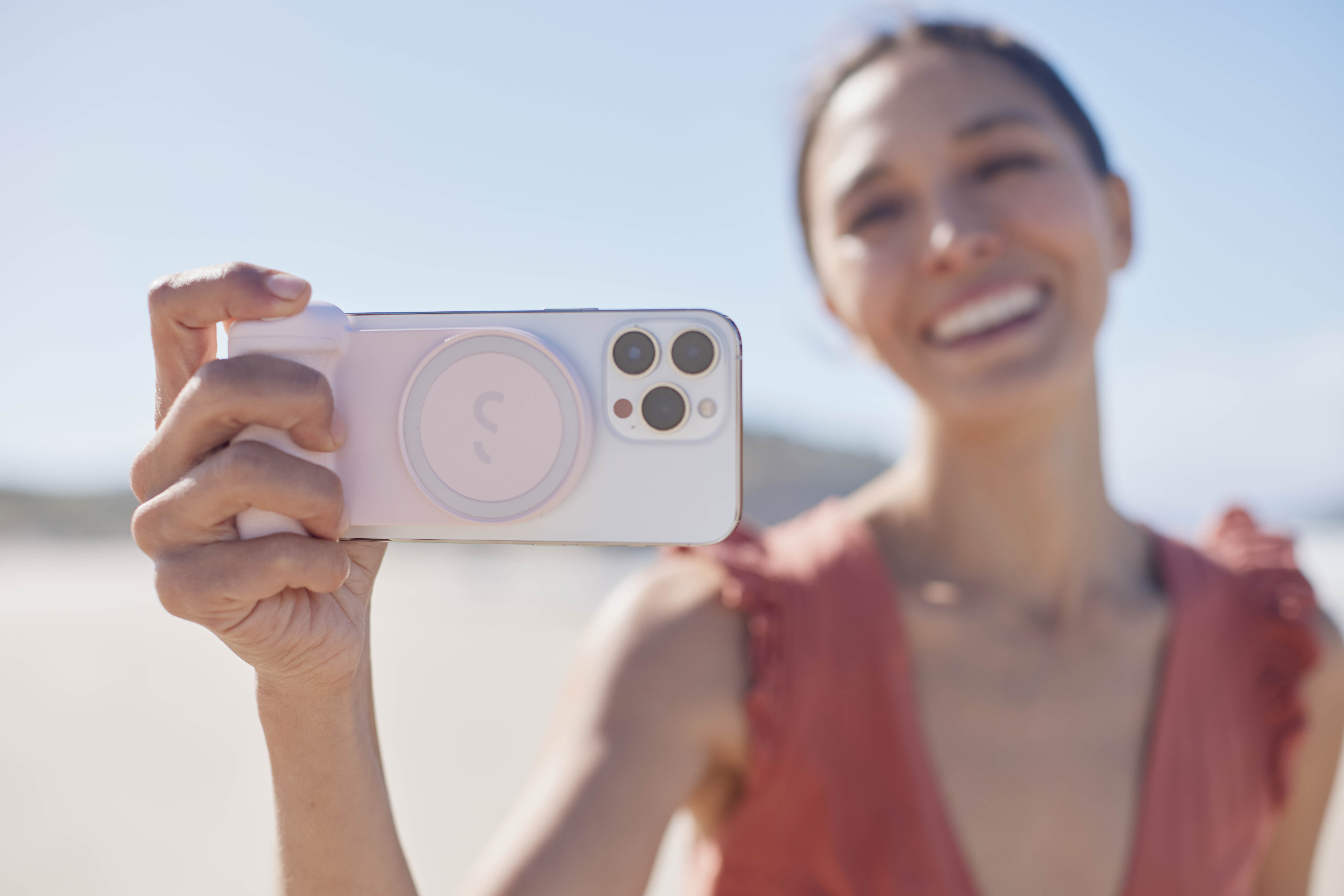 Frau macht Selfie am Strand, hält ein weißes und rosa Telefon.