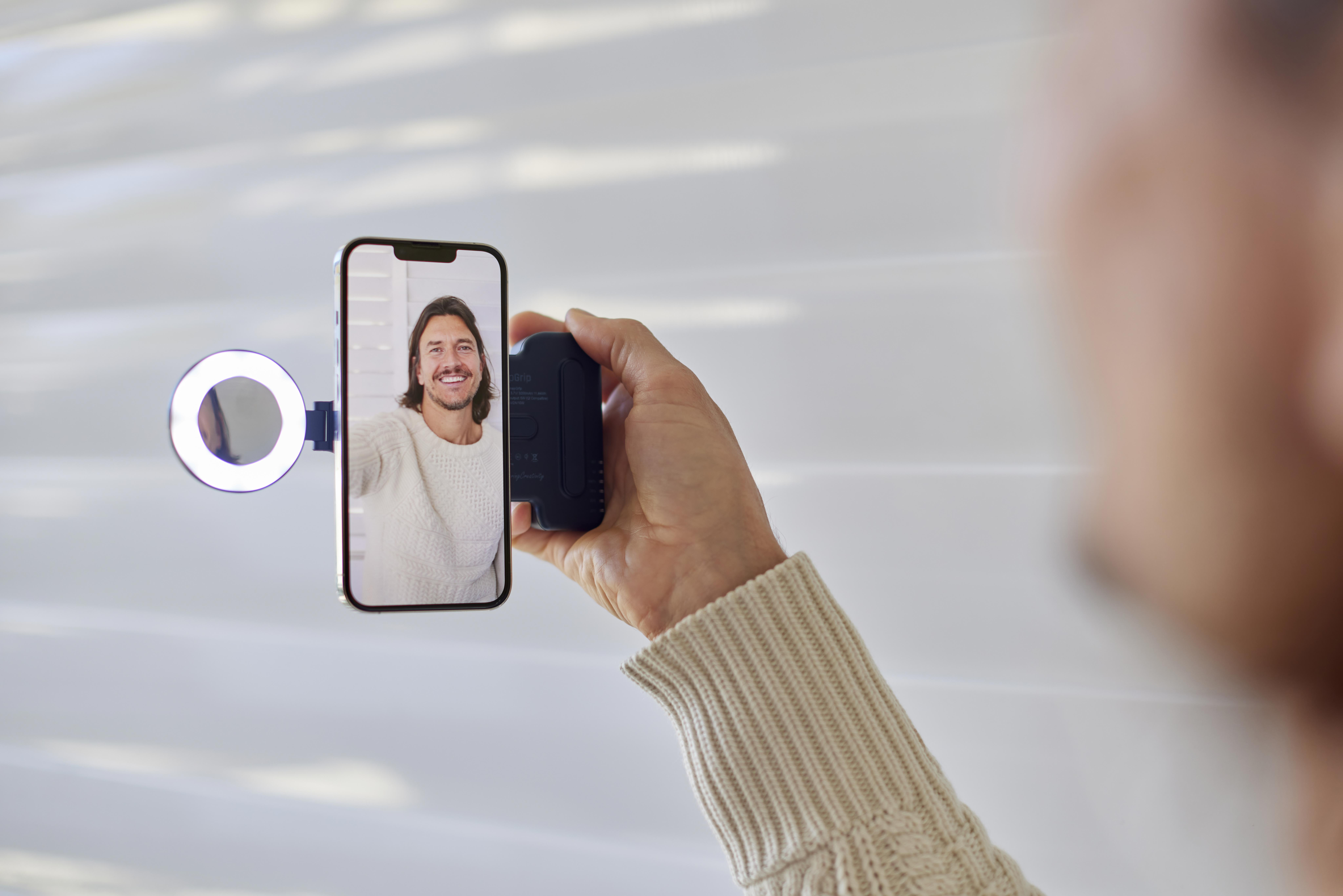 Person hält ein Telefon mit Selfie-Lichtaufsatz und zeigt das Gesicht einer Person auf dem Bildschirm.