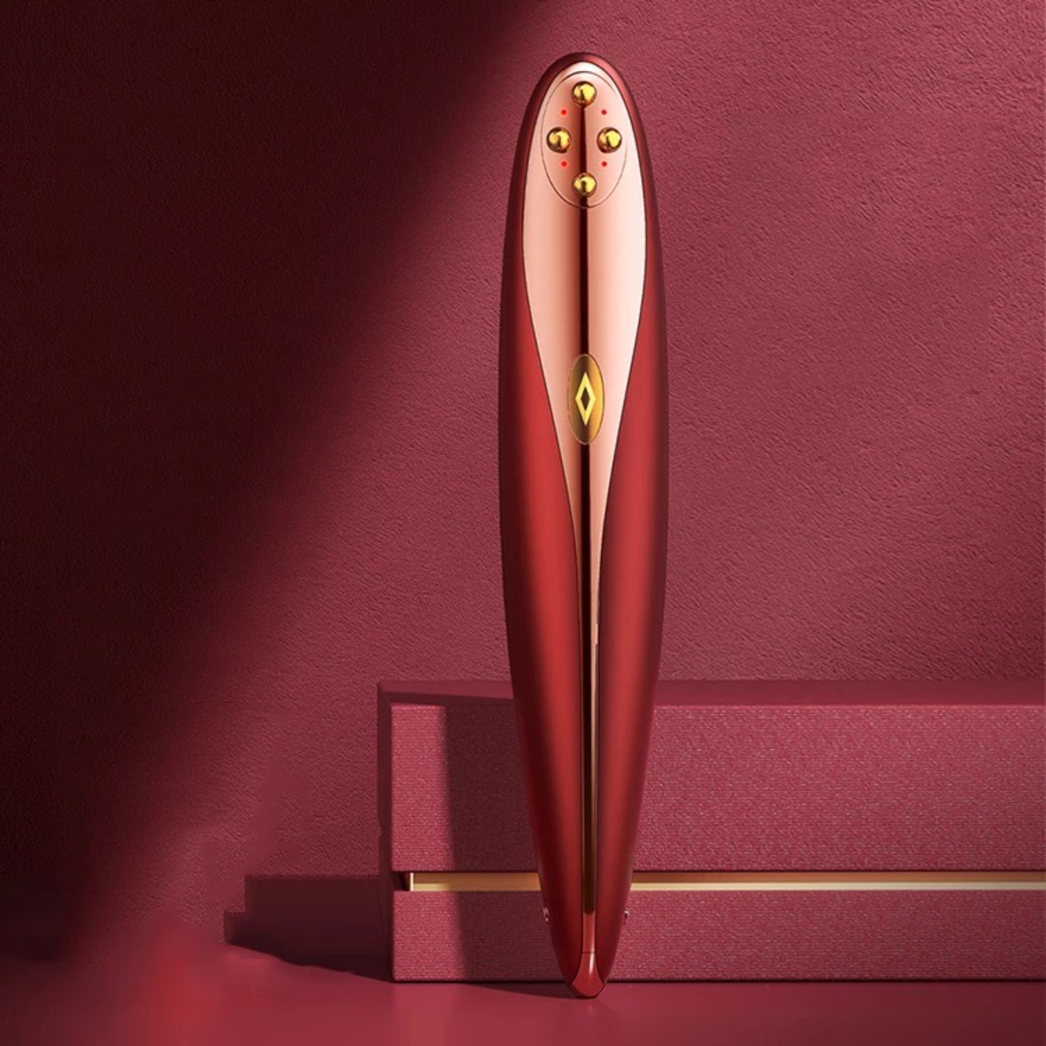 Czerwona, metaliczna zabawka erotyczna ze złotymi akcentami, prezentowana na teksturowanej czerwonej powierzchni.