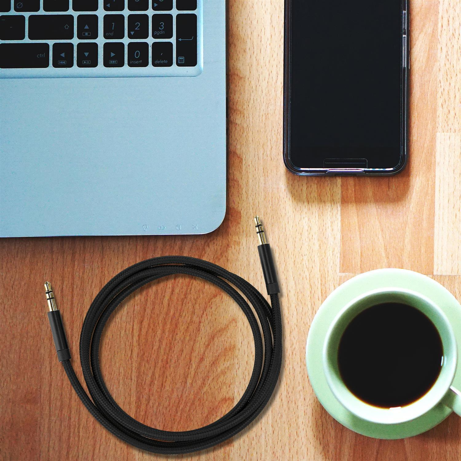Portátil, teléfono y taza de café con un cable de audio negro sobre una mesa de madera.
