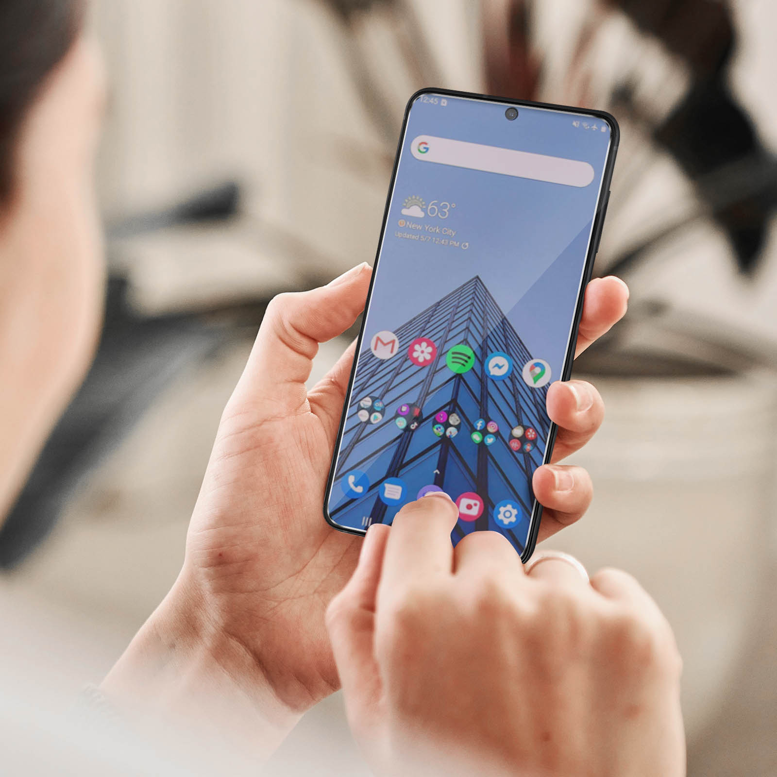 Una persona che tiene in mano uno smartphone con icone, un widget meteo e un edificio sullo schermo.