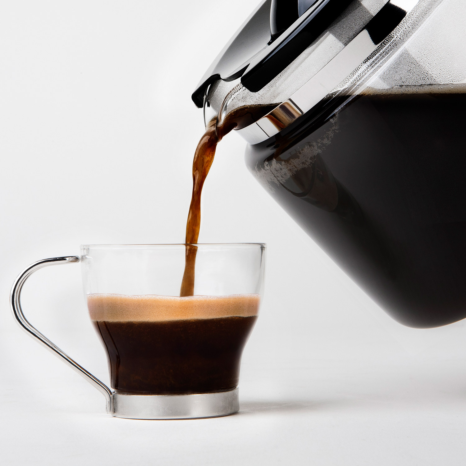 Przezroczysty szklany kubek napełniany ciemną kawą z dzbanka do kawy.