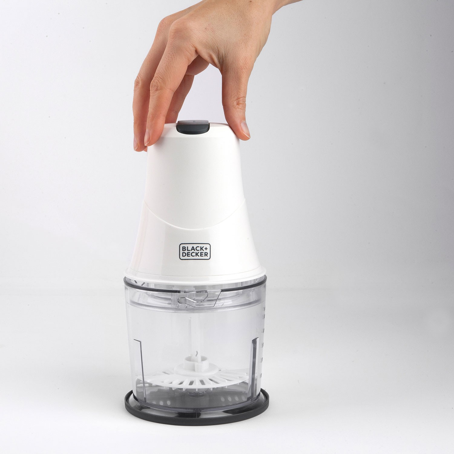 Tritatutto alimentare Black+Decker bianco. Ciotola trasparente, coperchio bianco e una mano. Sfondo bianco.