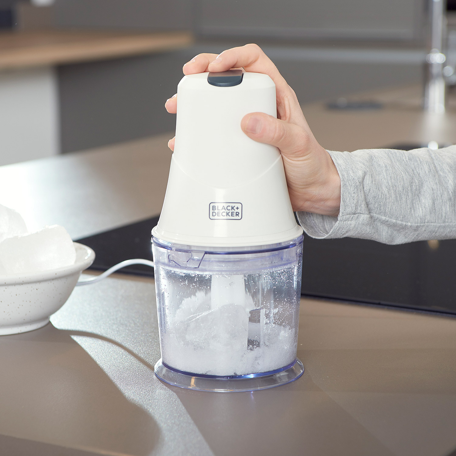 Tritatutto elettrico bianco con ghiaccio all'interno, tenuto da una mano. Bancone della cucina.