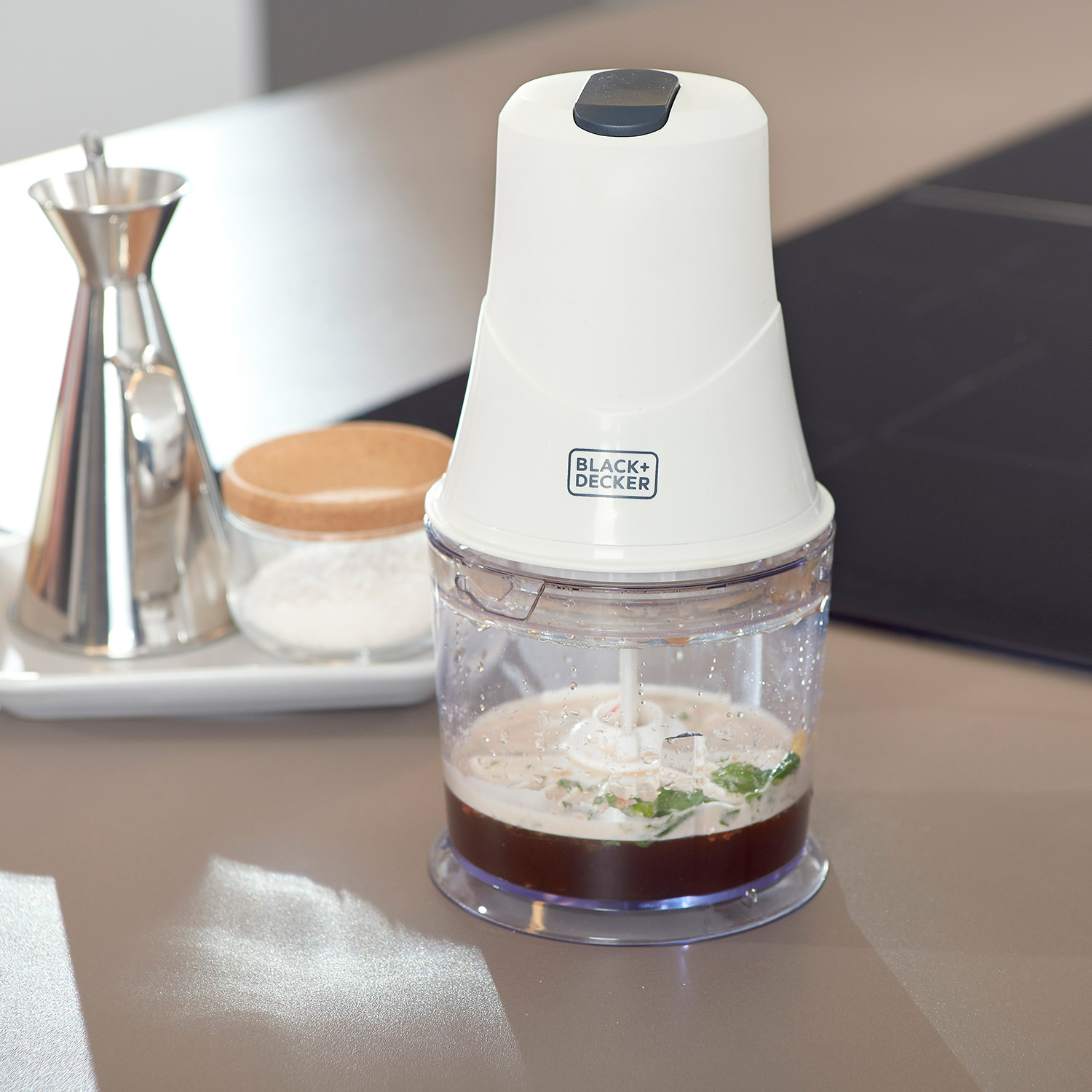 Tritatutto Black+Decker bianco e nero con ingredienti, su un piano di lavoro.