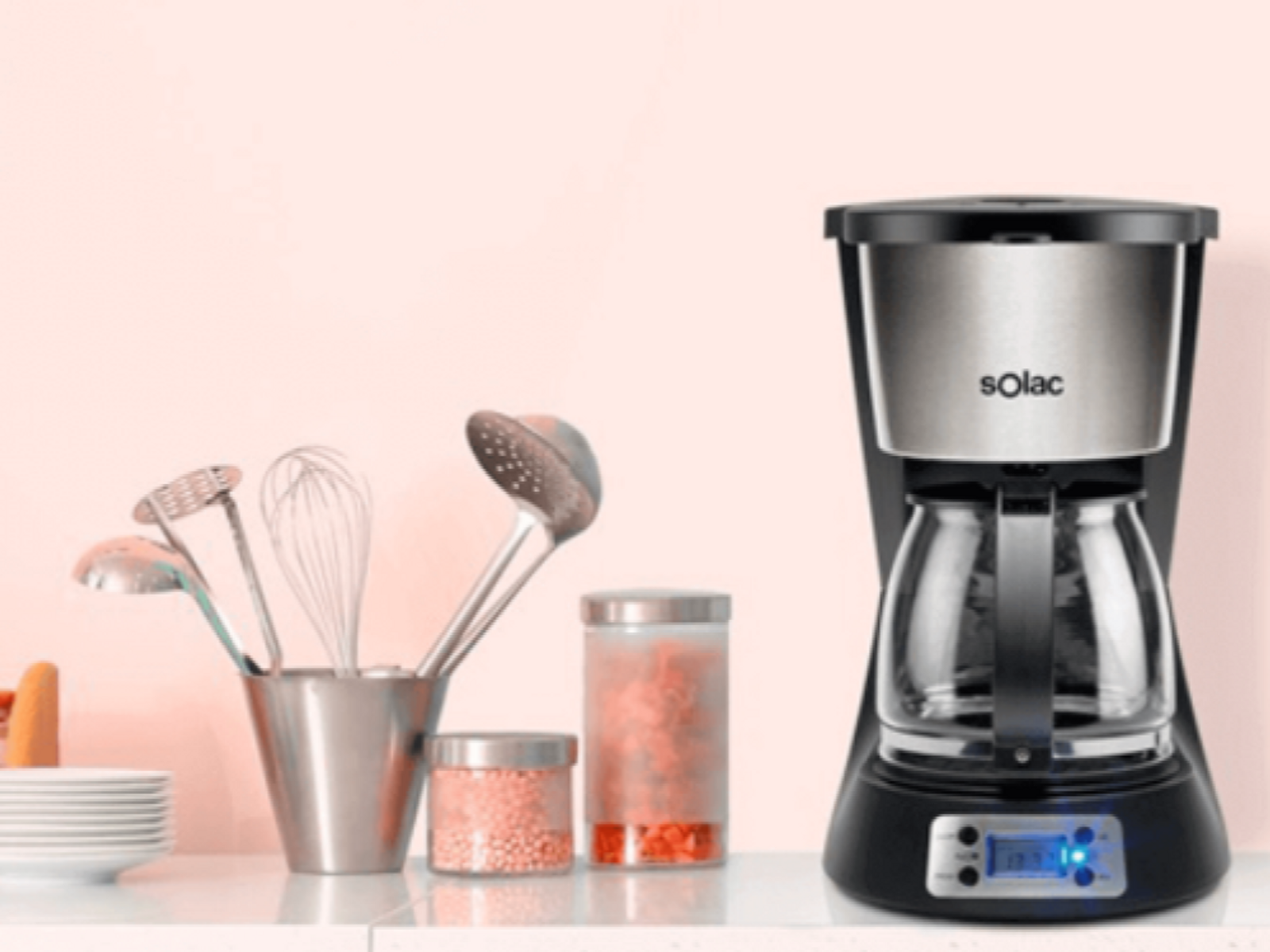 Una cafetera junto a utensilios de cocina y frascos con contenido rosa.