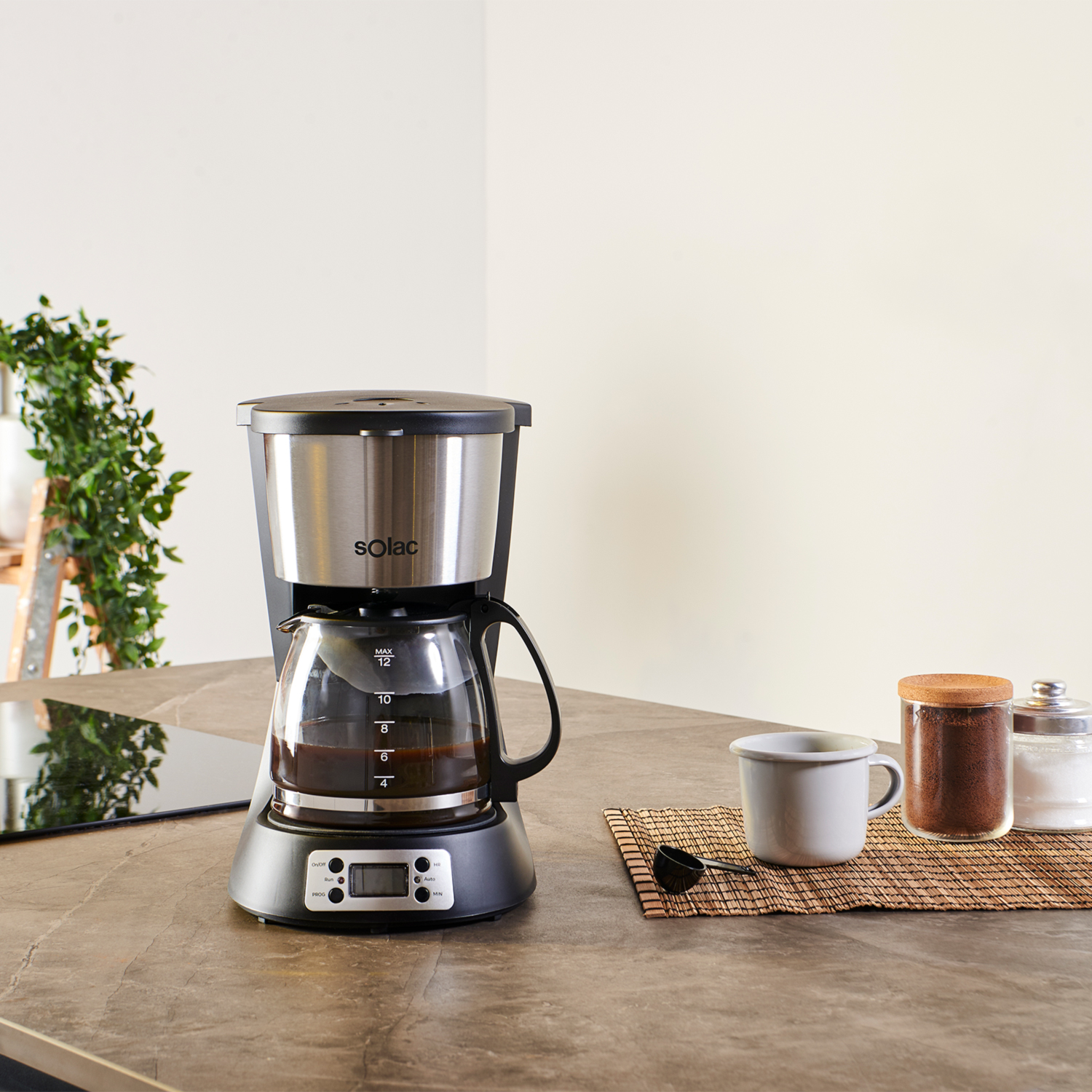 Cafetera con jarra de cristal, café en su interior. Taza y otros ingredientes en la encimera.