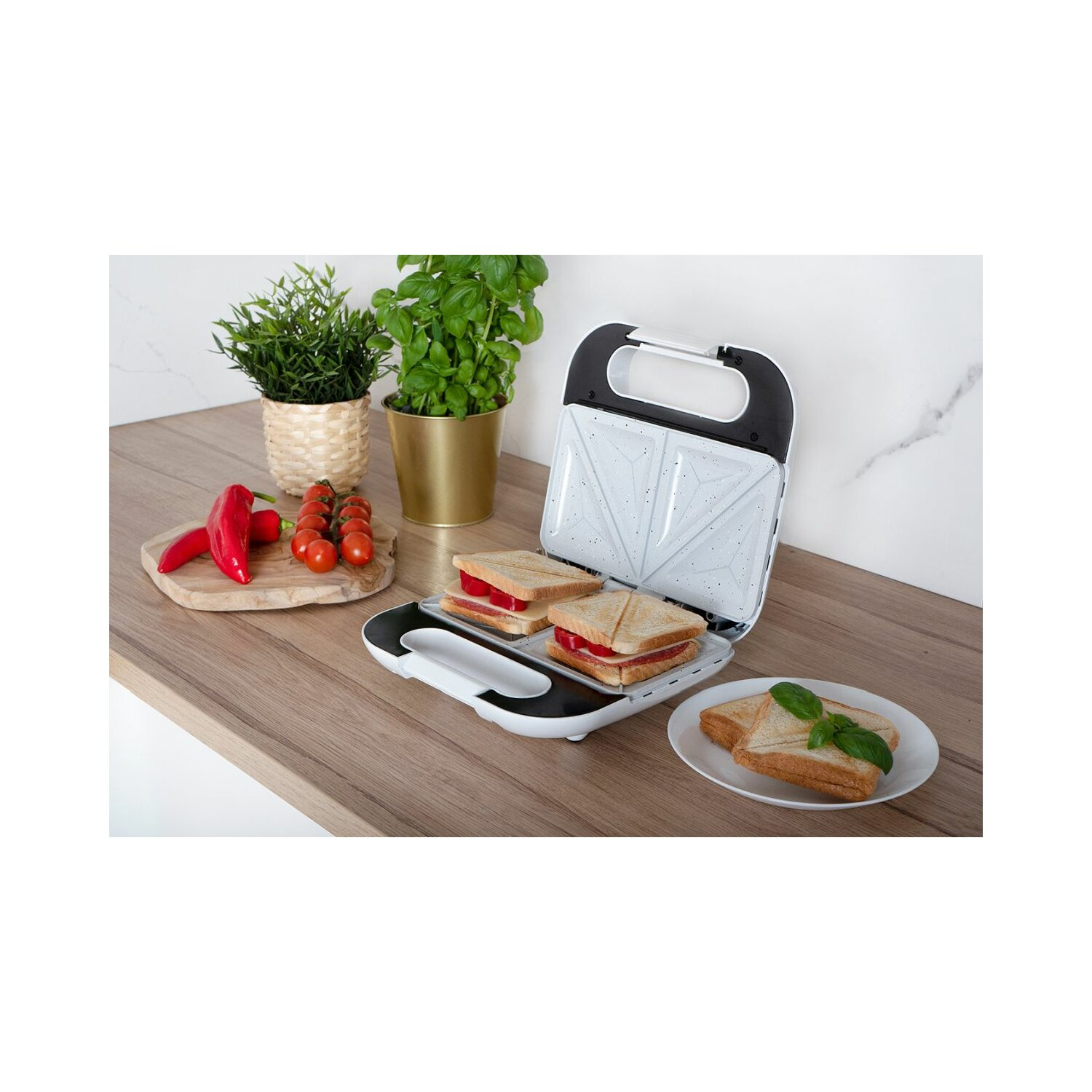 Ein Sandwichmaker mit 2 Sandwiches im Inneren und einem auf einem Teller. Gemüse ist ebenfalls vorhanden.