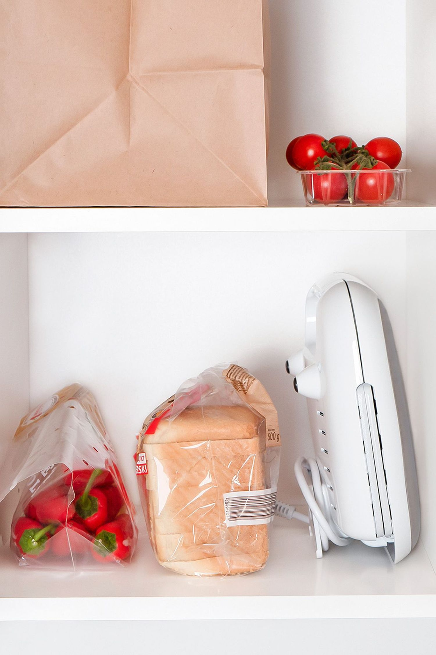 Ein Regal mit Lebensmitteln: Tomaten, Paprika, Brot und ein weißer Toaster.