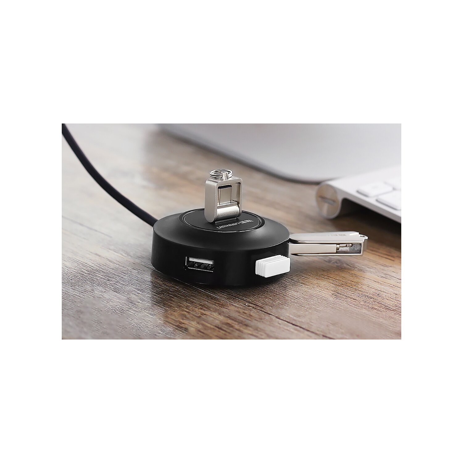 Schwarzer USB-Hub mit silberner Metallfeder und USB-Anschlüssen, mit Tastatur im Hintergrund.