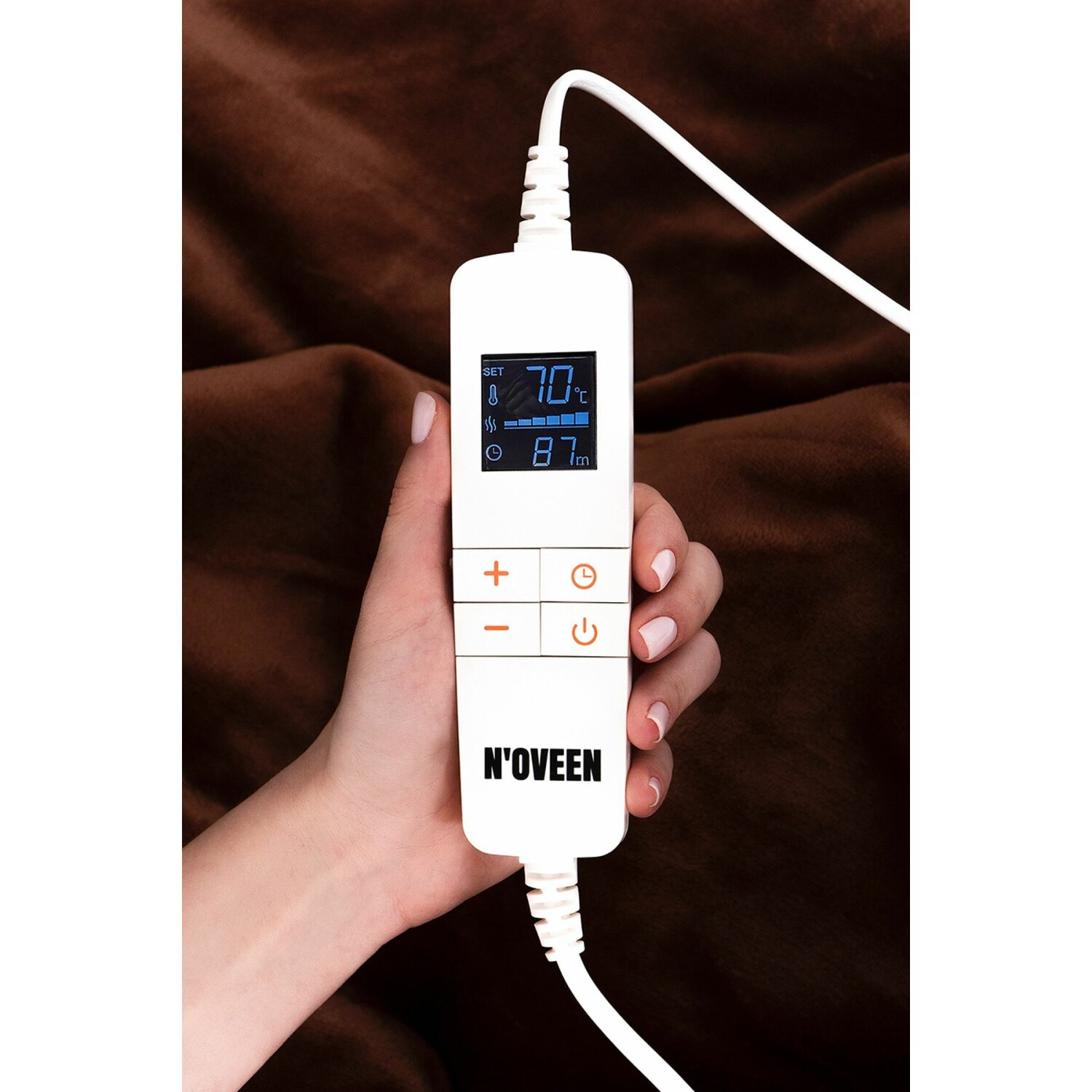 Eine Hand hält ein weißes Bedienfeld einer elektrischen Heizdecke, das Temperatur und Timer anzeigt.