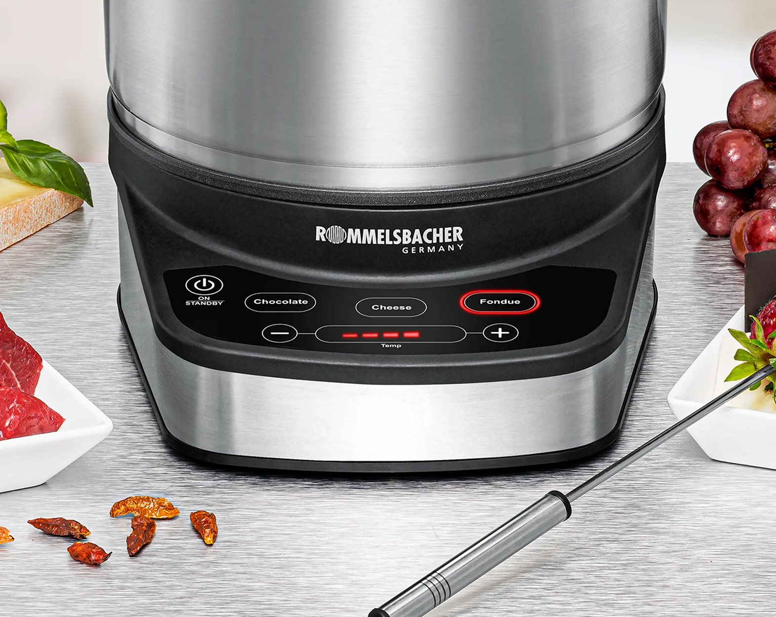 Eine Fondue-Maschine mit Lebensmitteln drumherum. Die Maschine hat ein Bedienfeld.