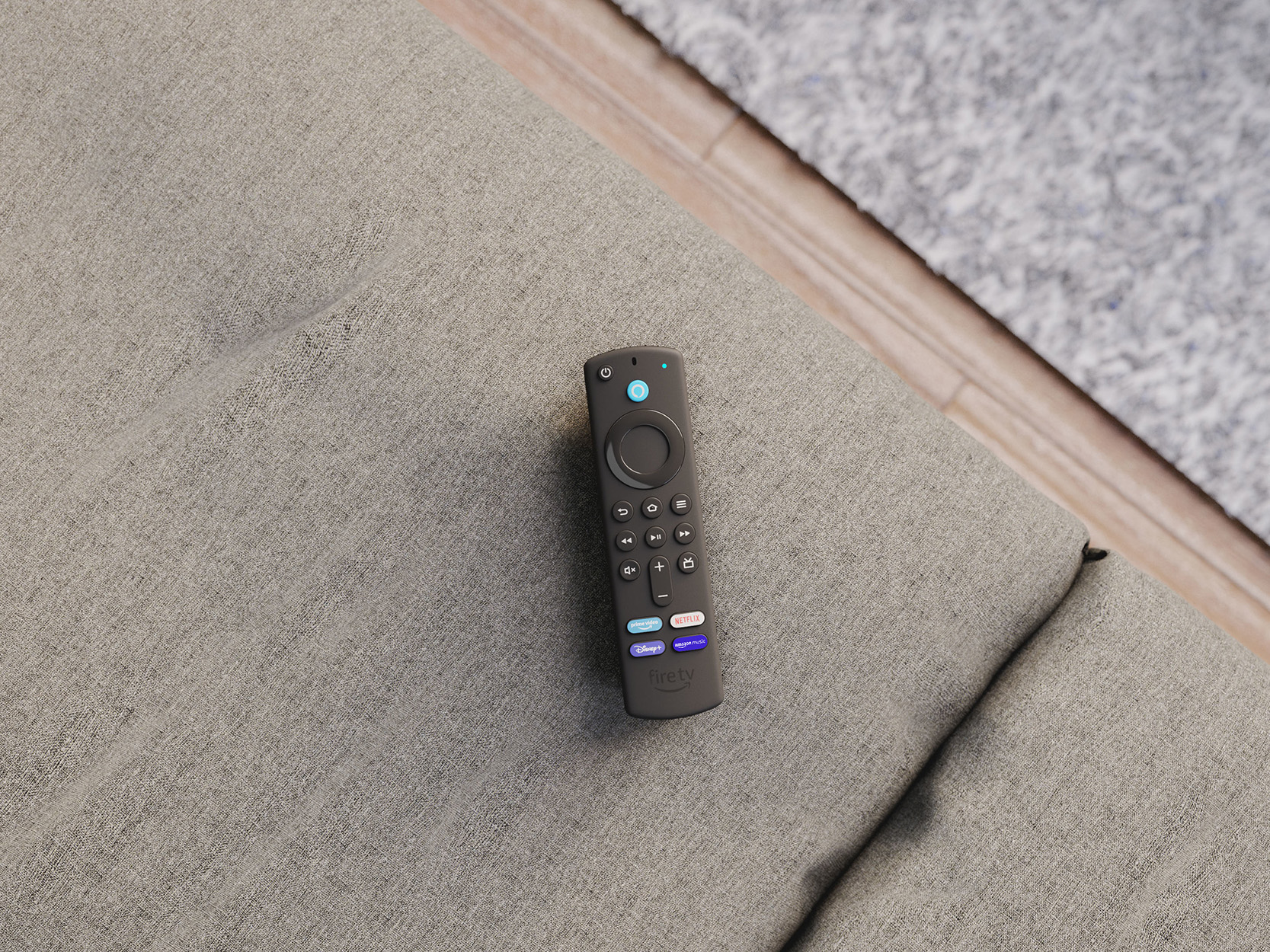 Schwarze Fire TV-Fernbedienung auf einer grauen Couch. Mehrere Tasten und Streaming-Dienste sichtbar.