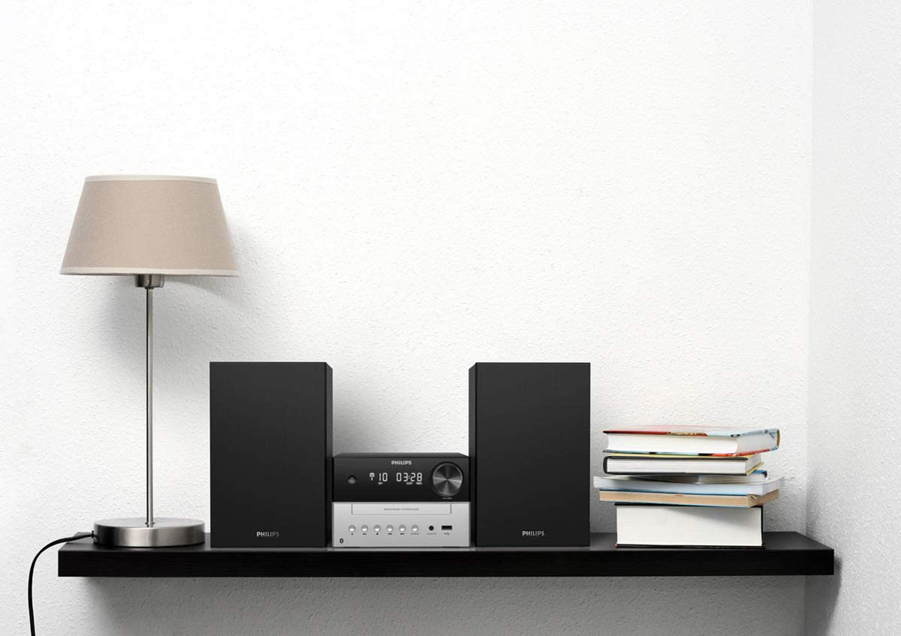Una mensola con lampada, altoparlanti, stereo e libri. Muro bianco sullo sfondo.