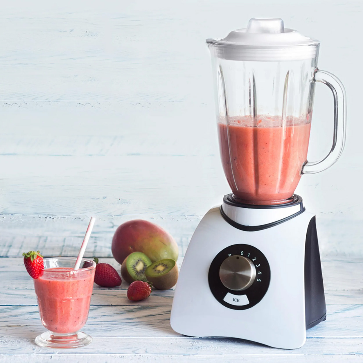 Mixer mit rotem Smoothie, Glas mit Smoothie, Erdbeeren, Kiwi und Mango.