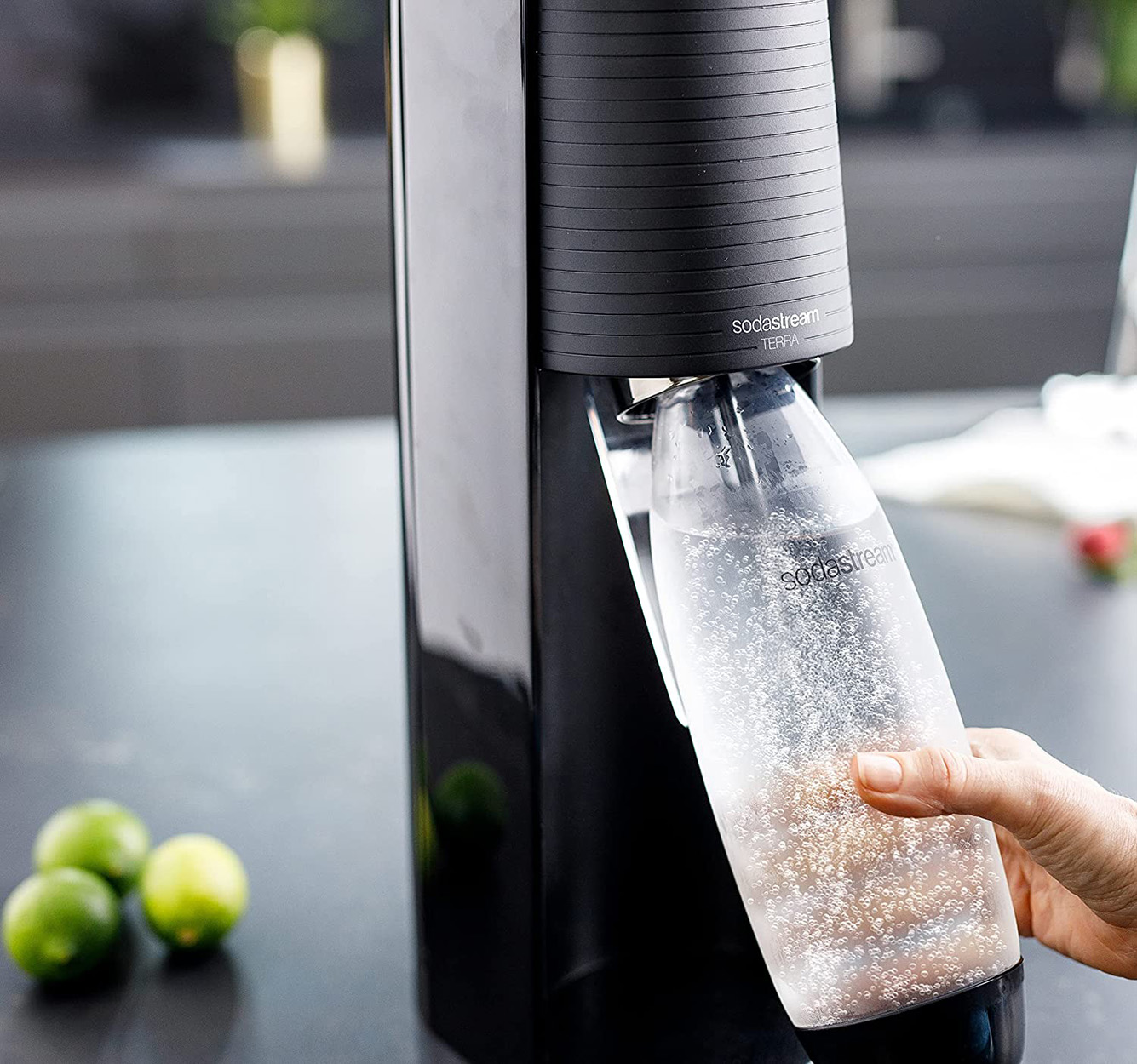Macchina SodaStream con una bottiglia di acqua frizzante, lime e la mano di una persona.